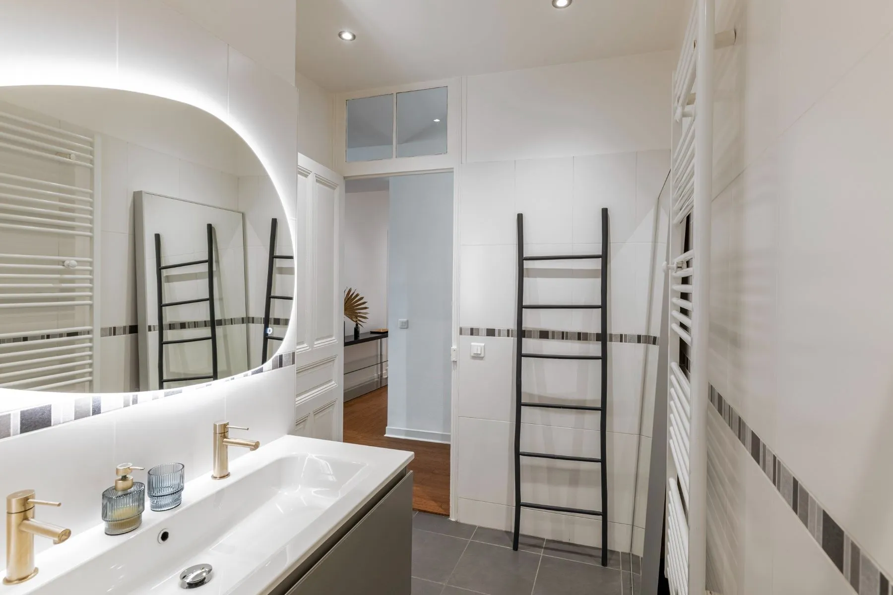 White-tiled bathroom with illuminated mirror, gold-toned taps and heated towel rail