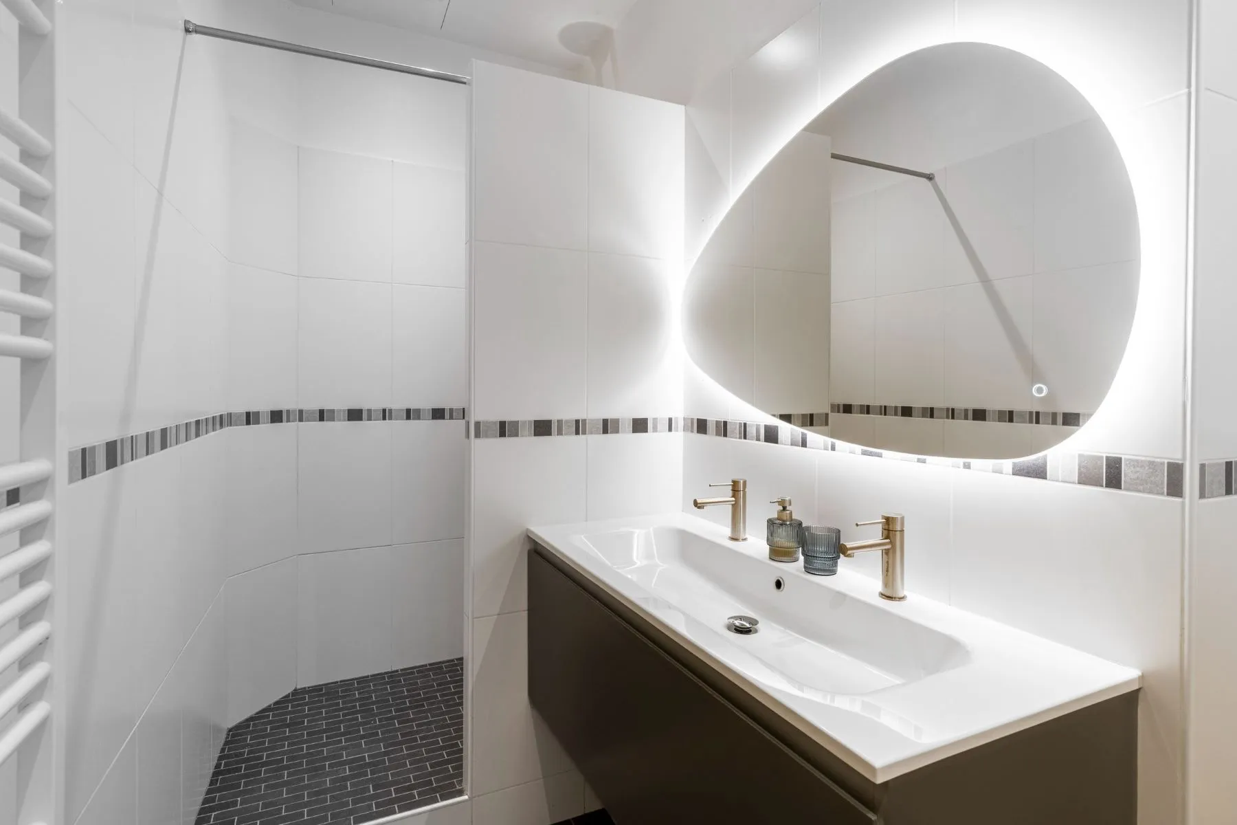 Bathroom vanity with illuminated sculptural mirror and gold-toned fittings