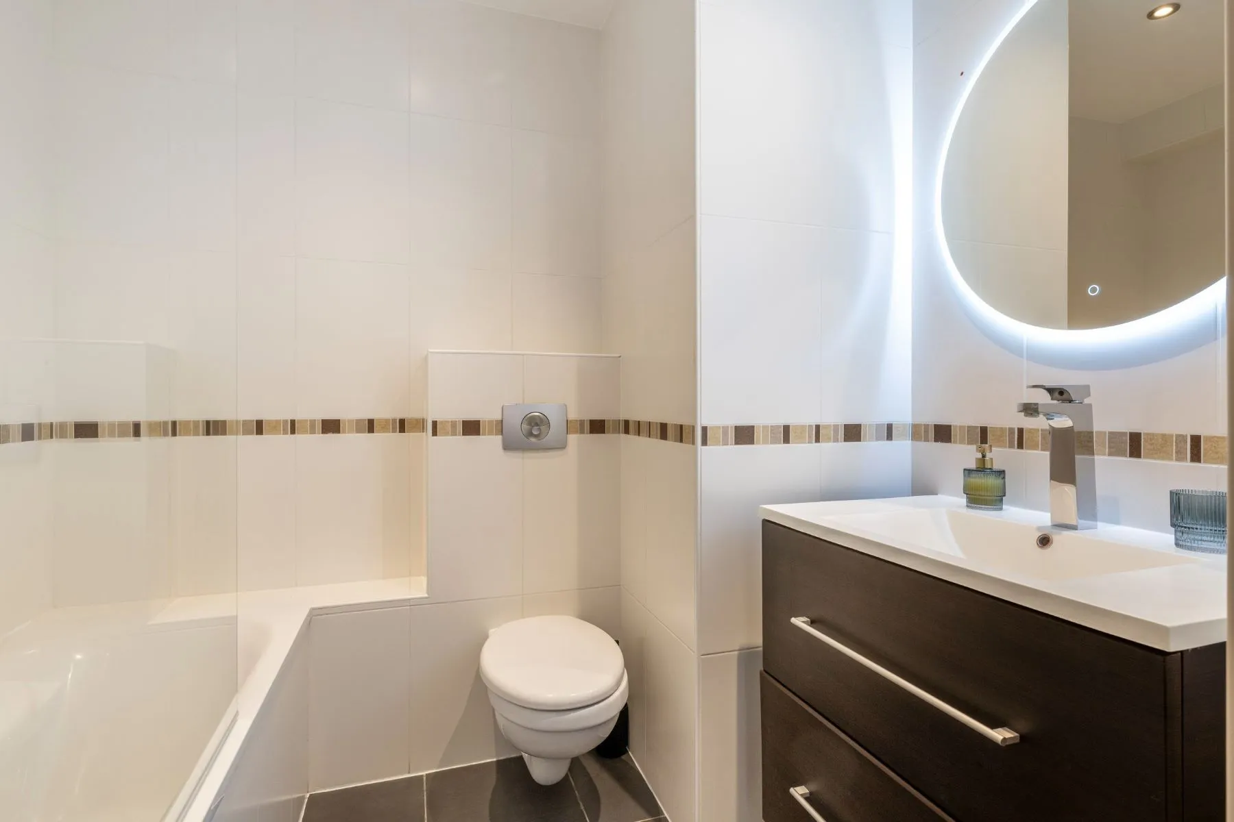 Second bathroom with bathtub, toilet and dark vanity beneath an illuminated mirror