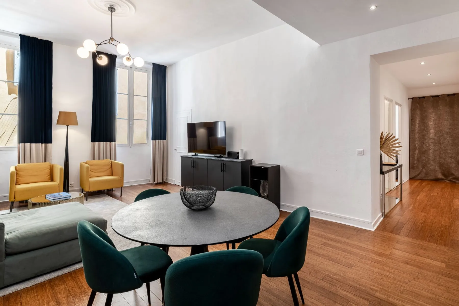 Round dining table and green upholstered chairs beside the bright high-ceilinged lounge