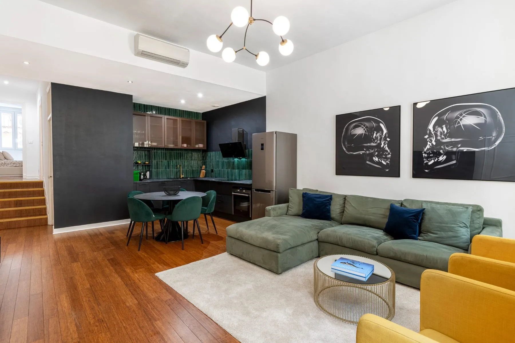 Green corner sofa and open kitchen with dark cabinetry and emerald tile splashback