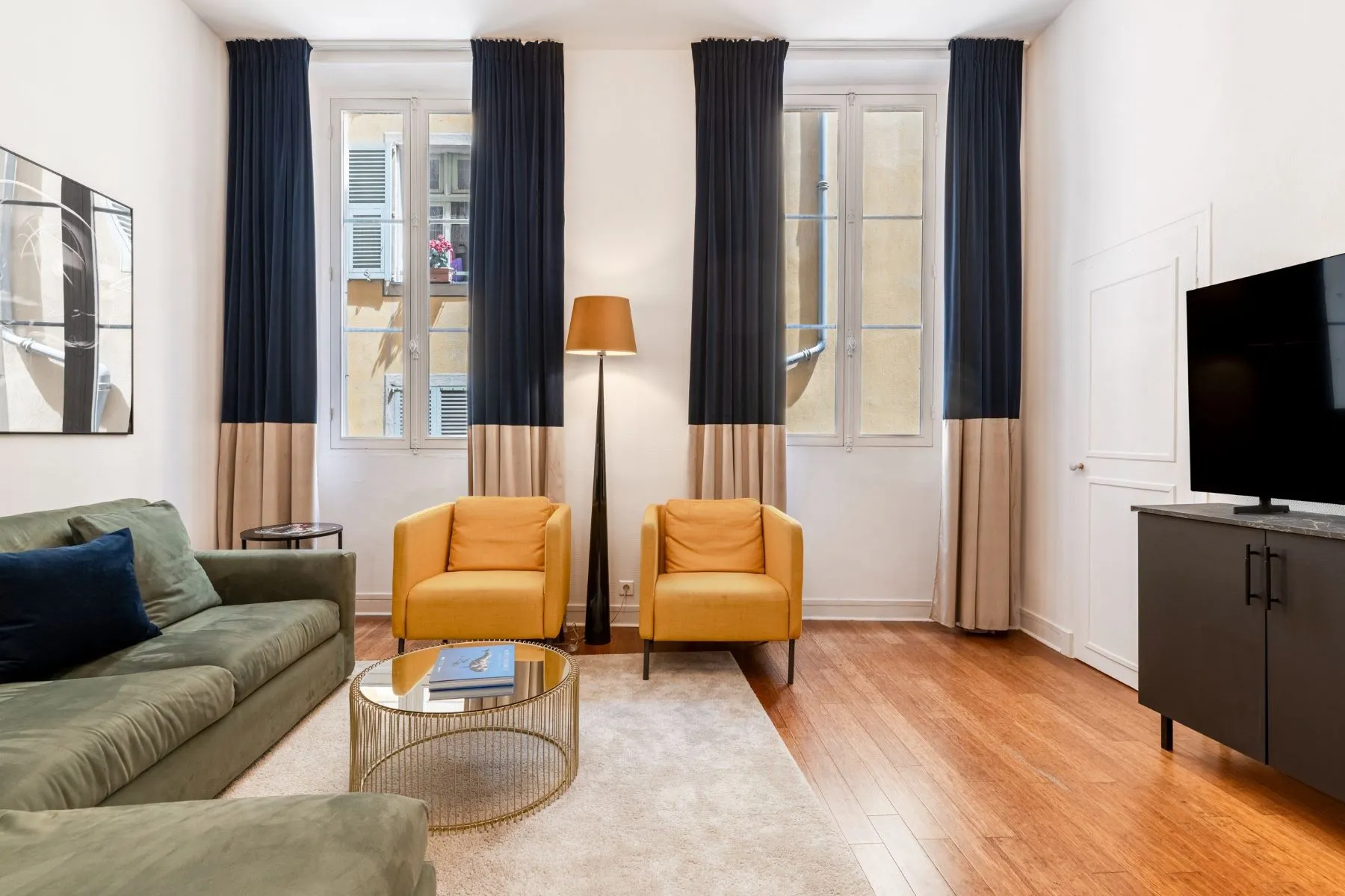 Sunlit lounge with tall French windows, mustard armchairs and living-room television