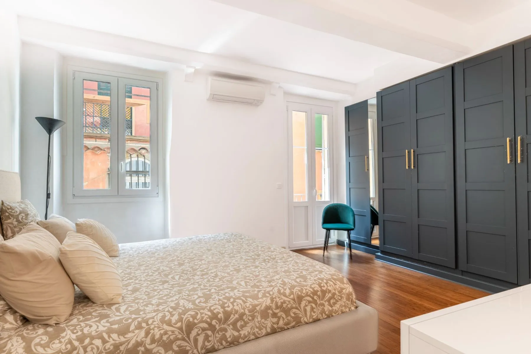 Spacious double bedroom with dark fitted wardrobes, timber floor and tall windows
