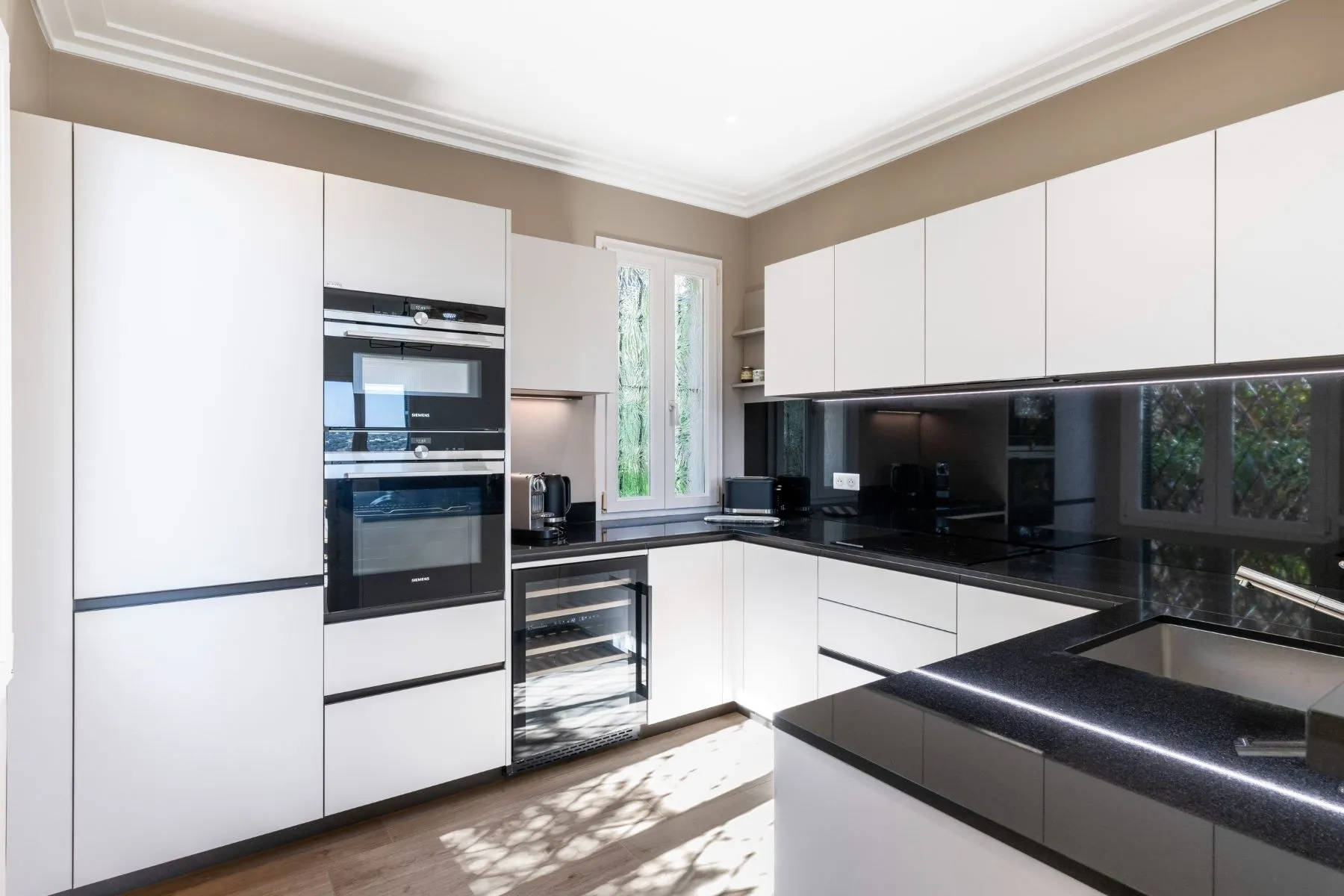 White fitted kitchen with black worktops, integrated cooking appliances and glass-fronted wine cooler