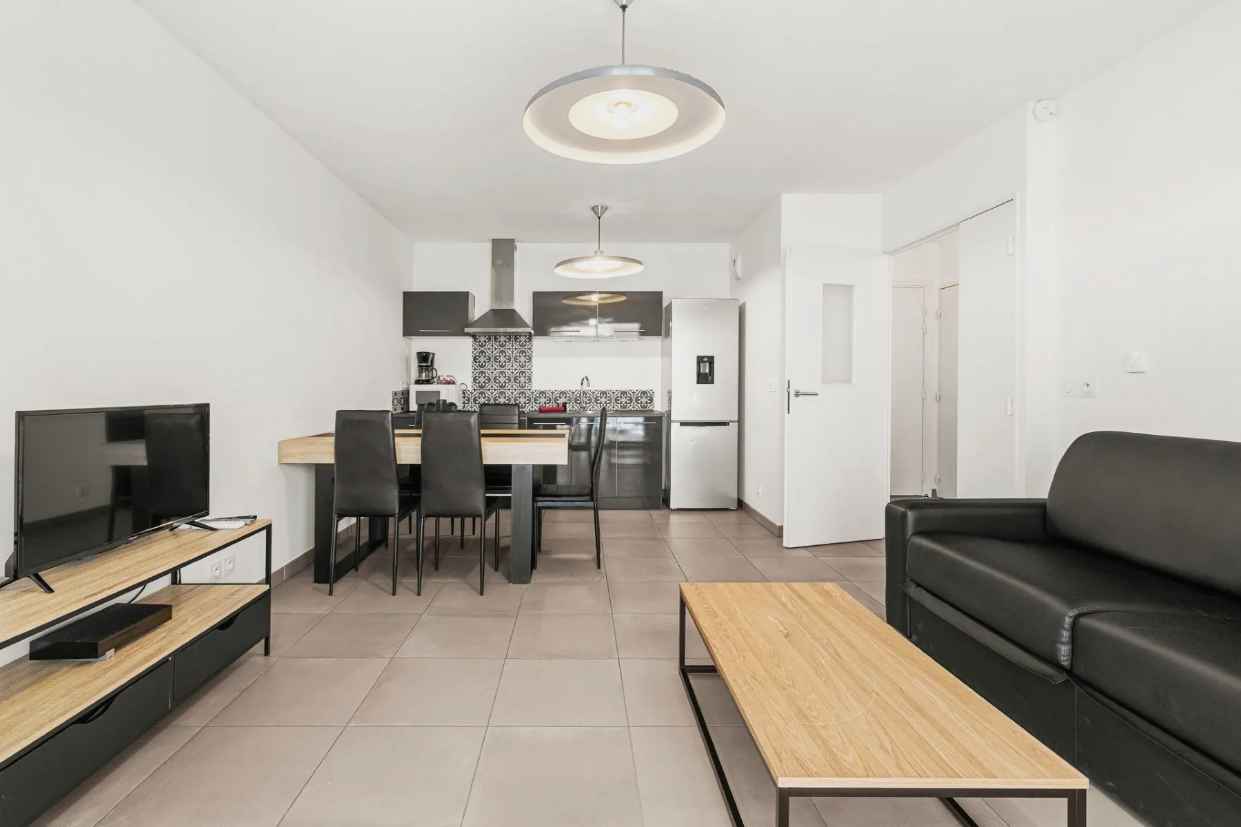 Nice open-plan living and dining room with black sofa, timber table and fitted kitchen