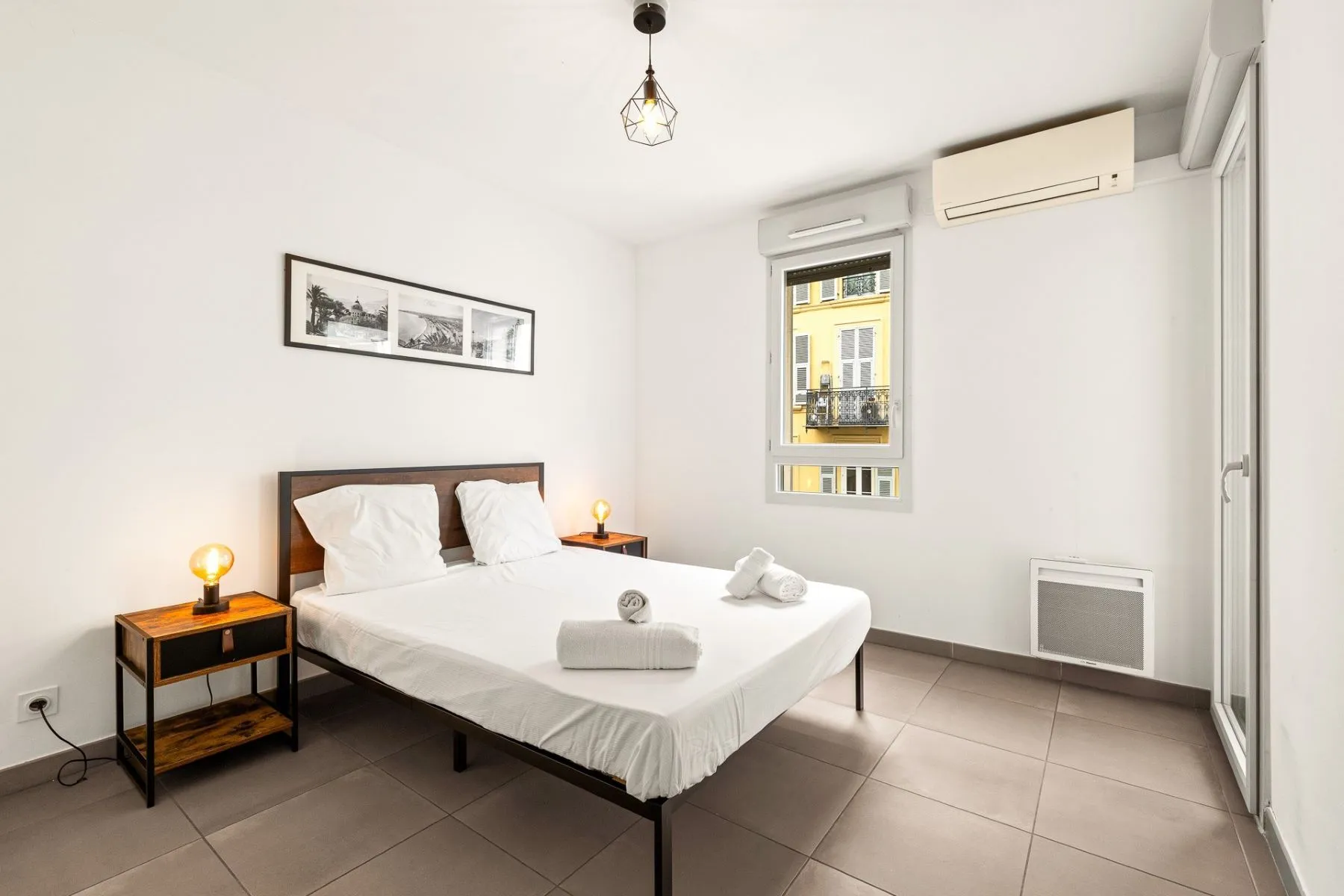 Double bedroom with white bedding, bedside lamps, air conditioning and a bright window
