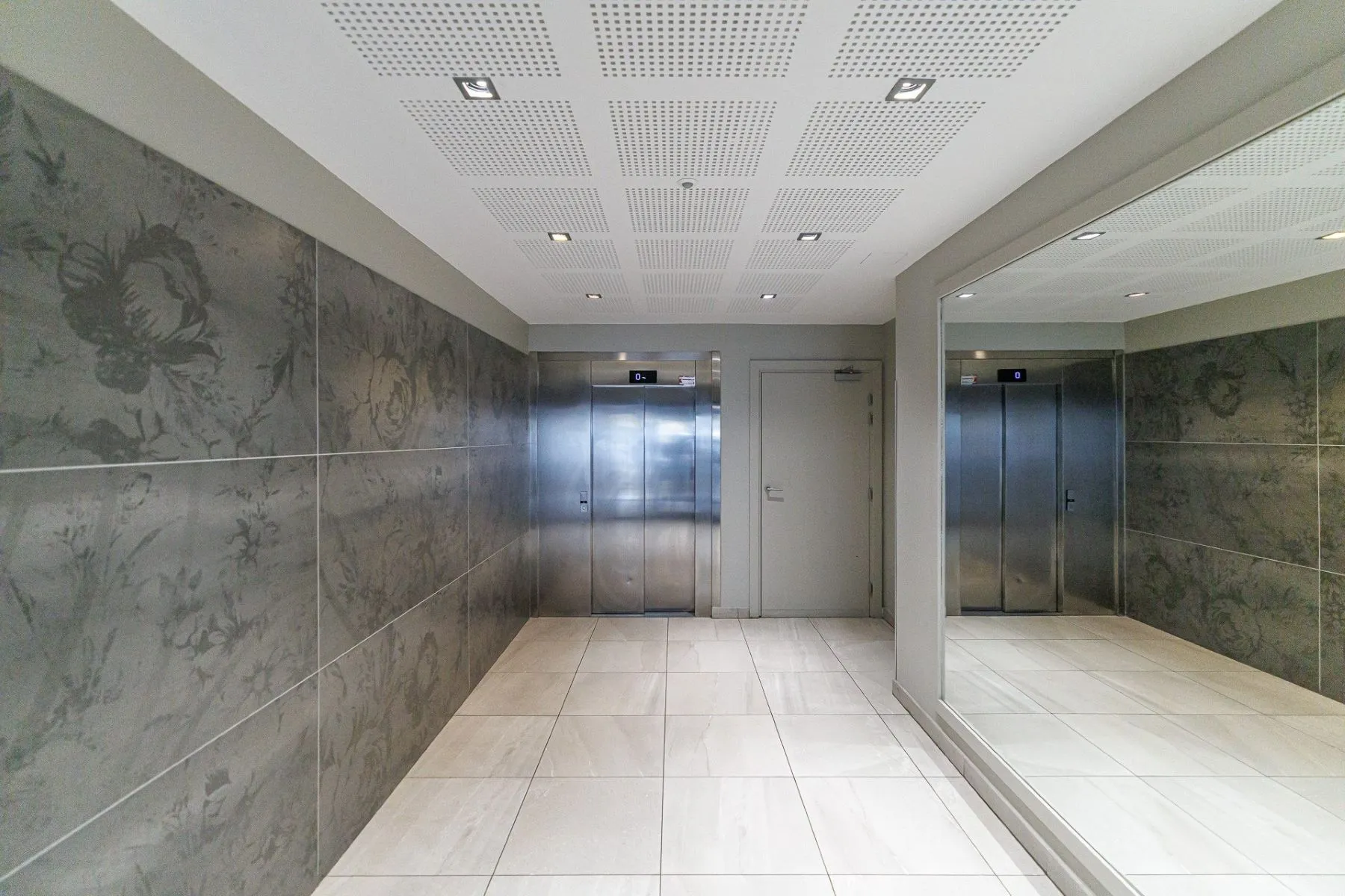 Modern communal lift lobby with decorative wall panels and recessed lighting