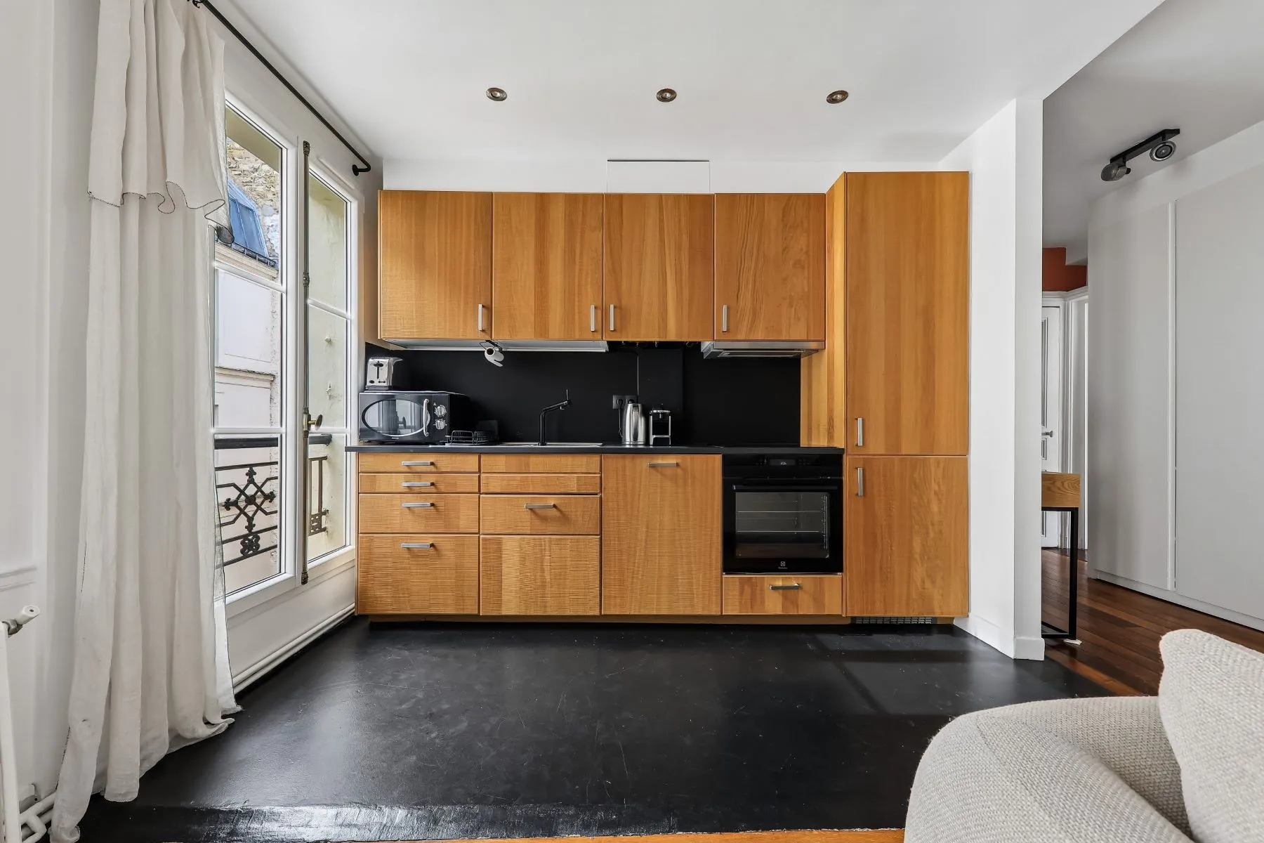 Timber fitted kitchen with black splashback, built-in oven and tall neighbouring window
