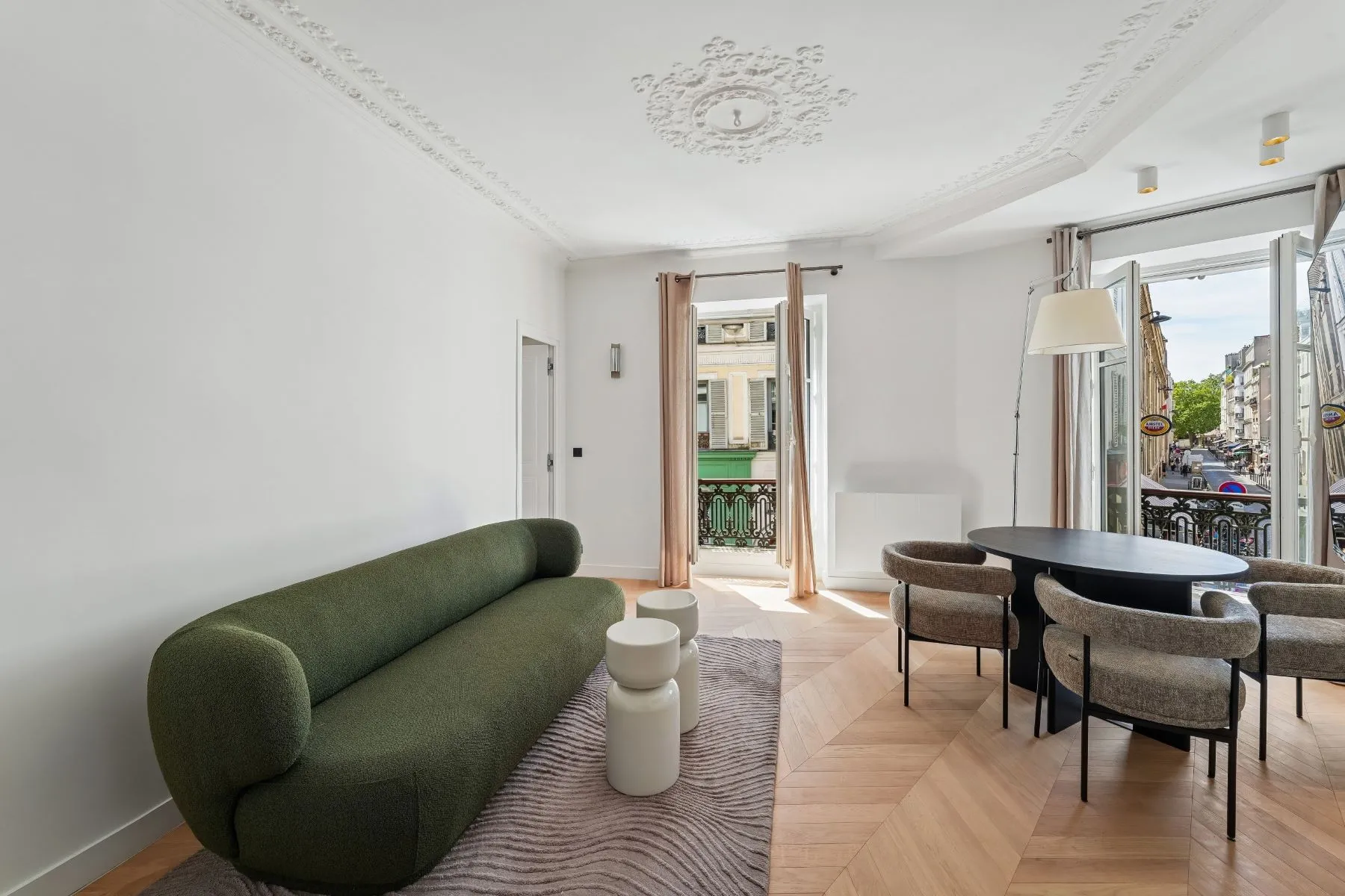 Bright Parisian lounge with curved green sofa and round dining table beside tall windows