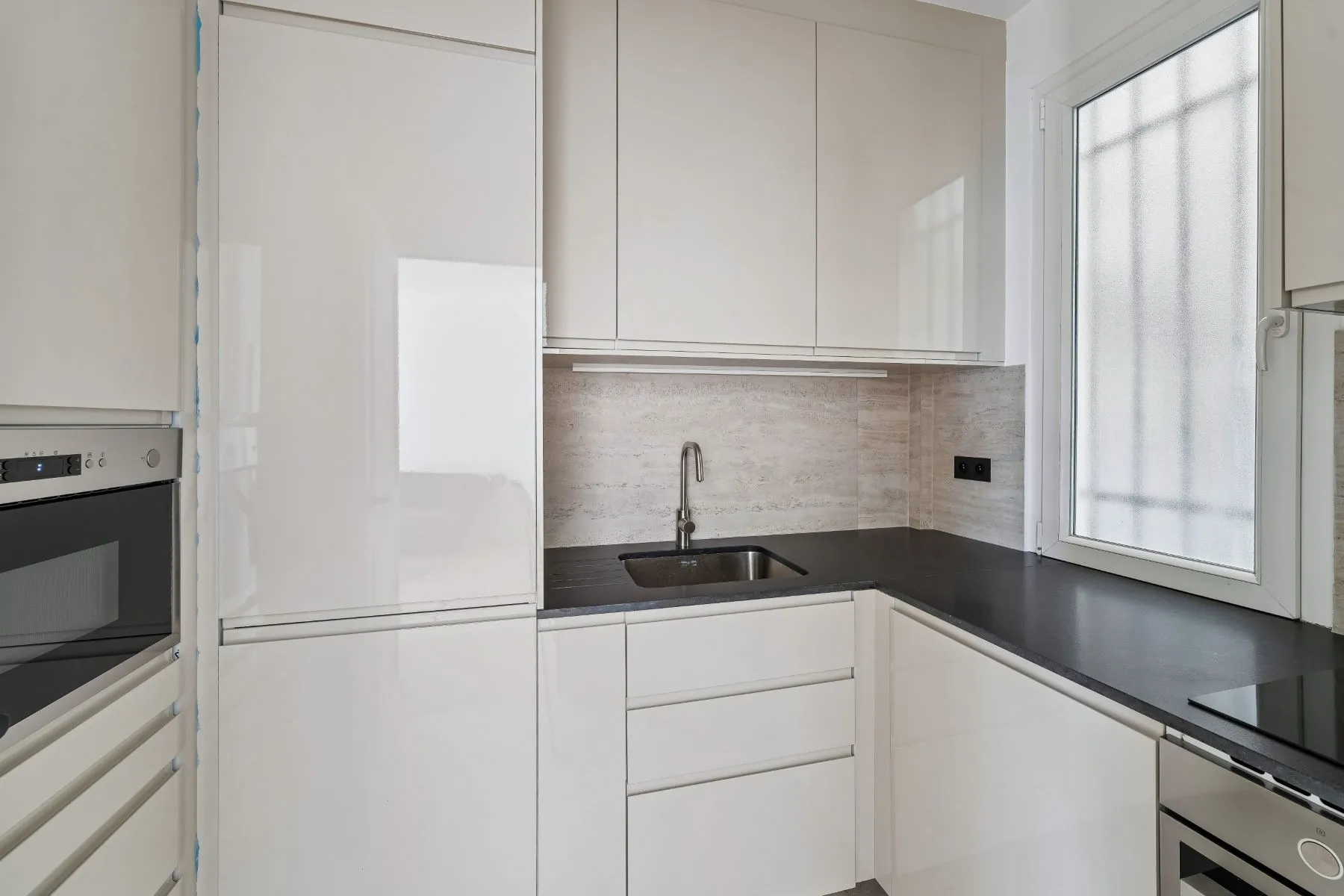 Separate fitted kitchen with white cabinetry, dark worktops and built-in oven
