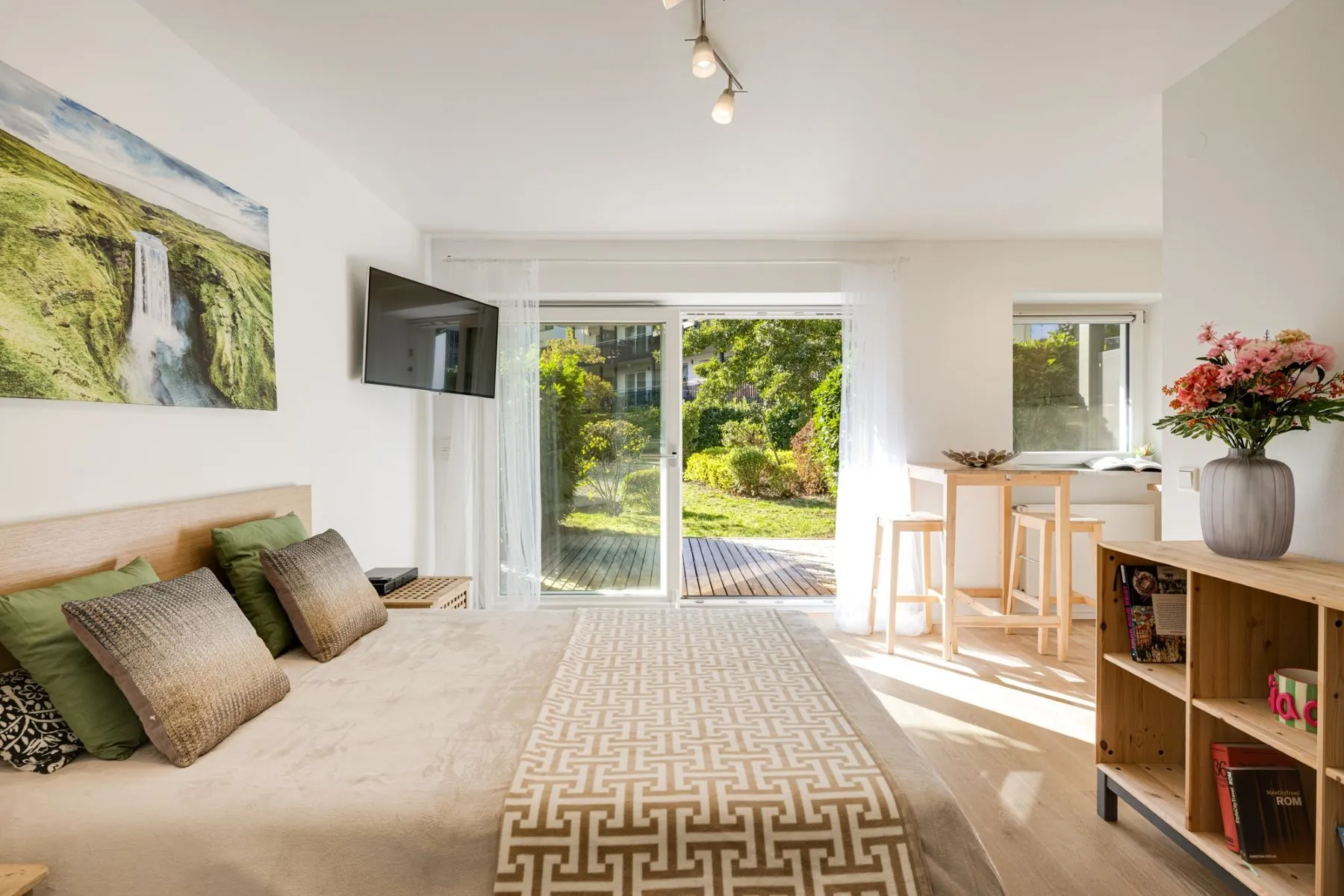 Bright studio sleeping area with double bed, wall-mounted television and garden doors