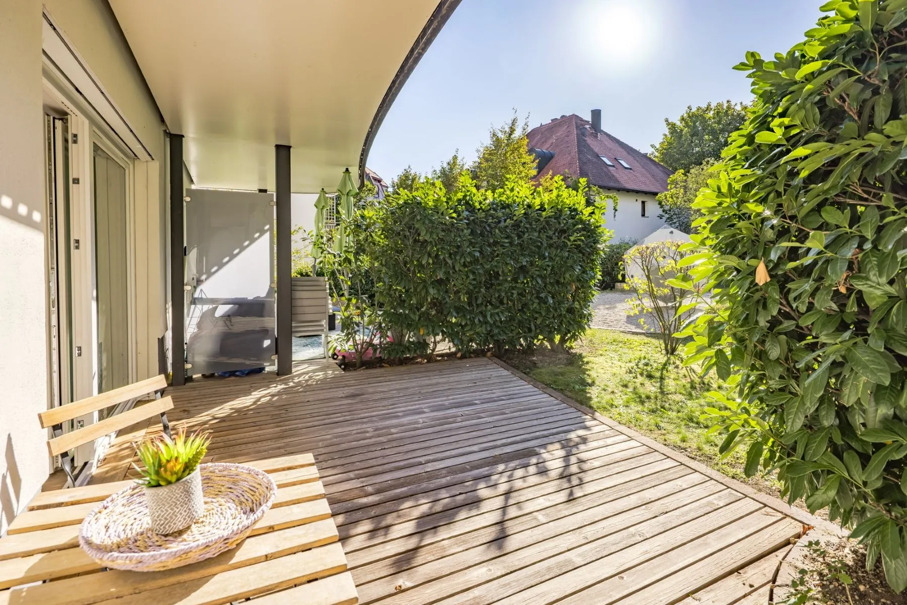 Sheltered wooden terrace with bistro table and hedges bordering the private garden