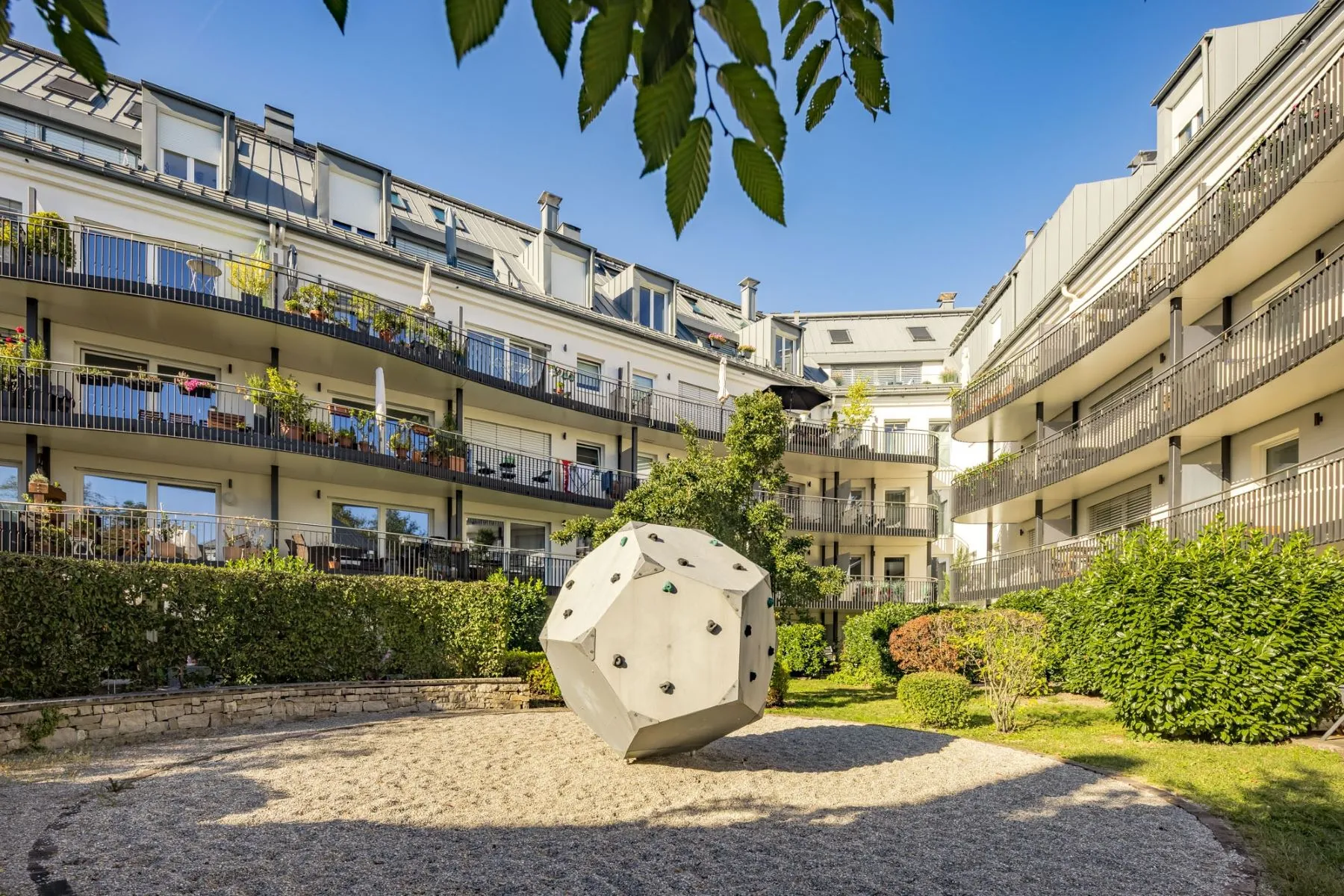 Landscaped residential courtyard with climbing boulder and surrounding balconies