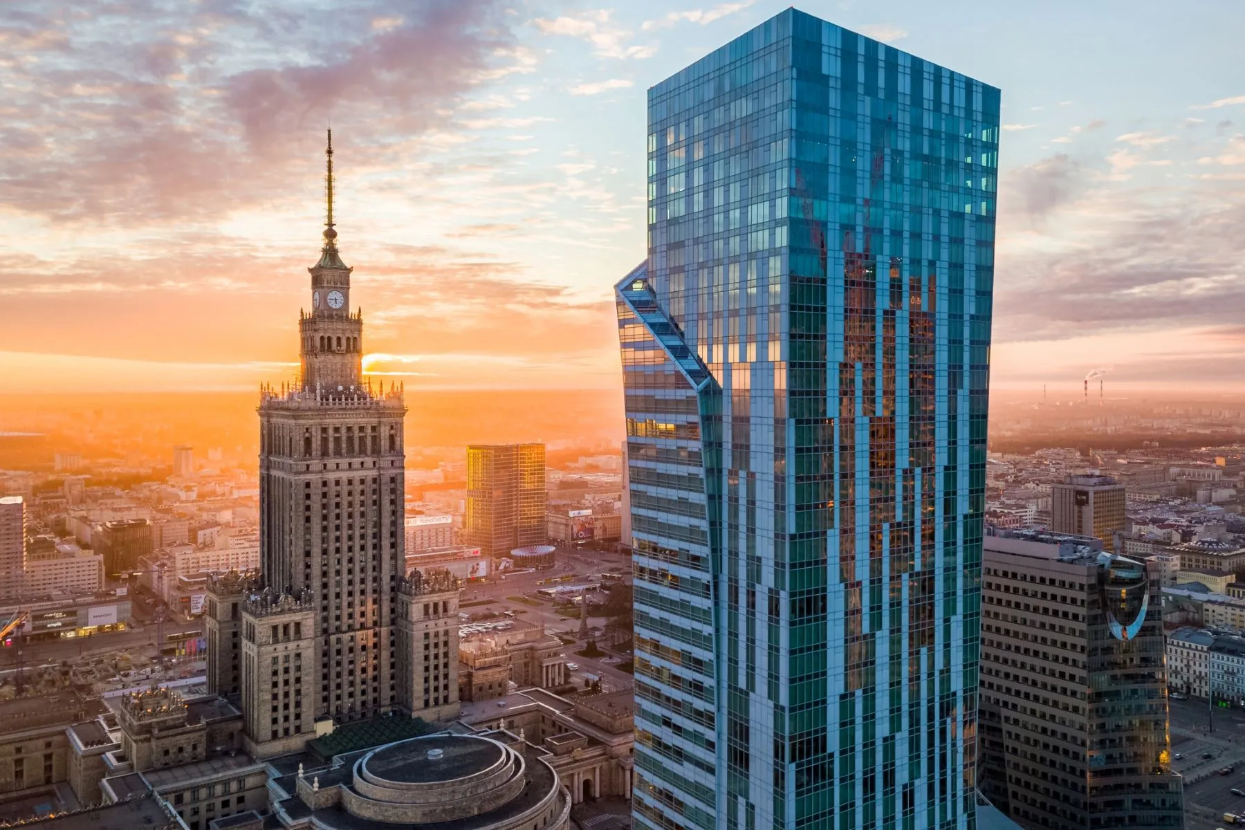 Golden-hour view of Warsaw’s modern towers beside the Palace of Culture and Science