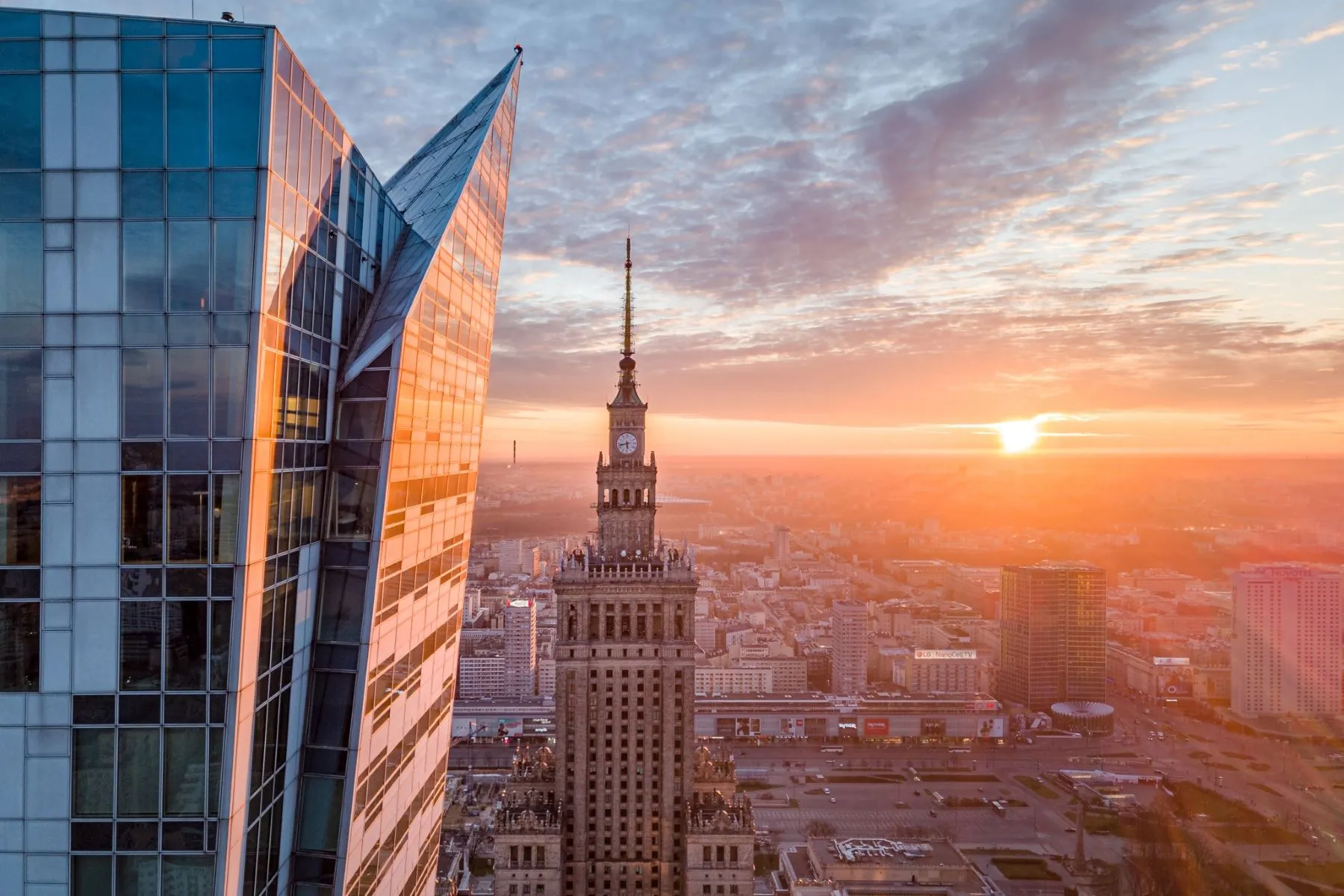 Angular glass architecture and the Palace of Culture and Science against a sunset sky
