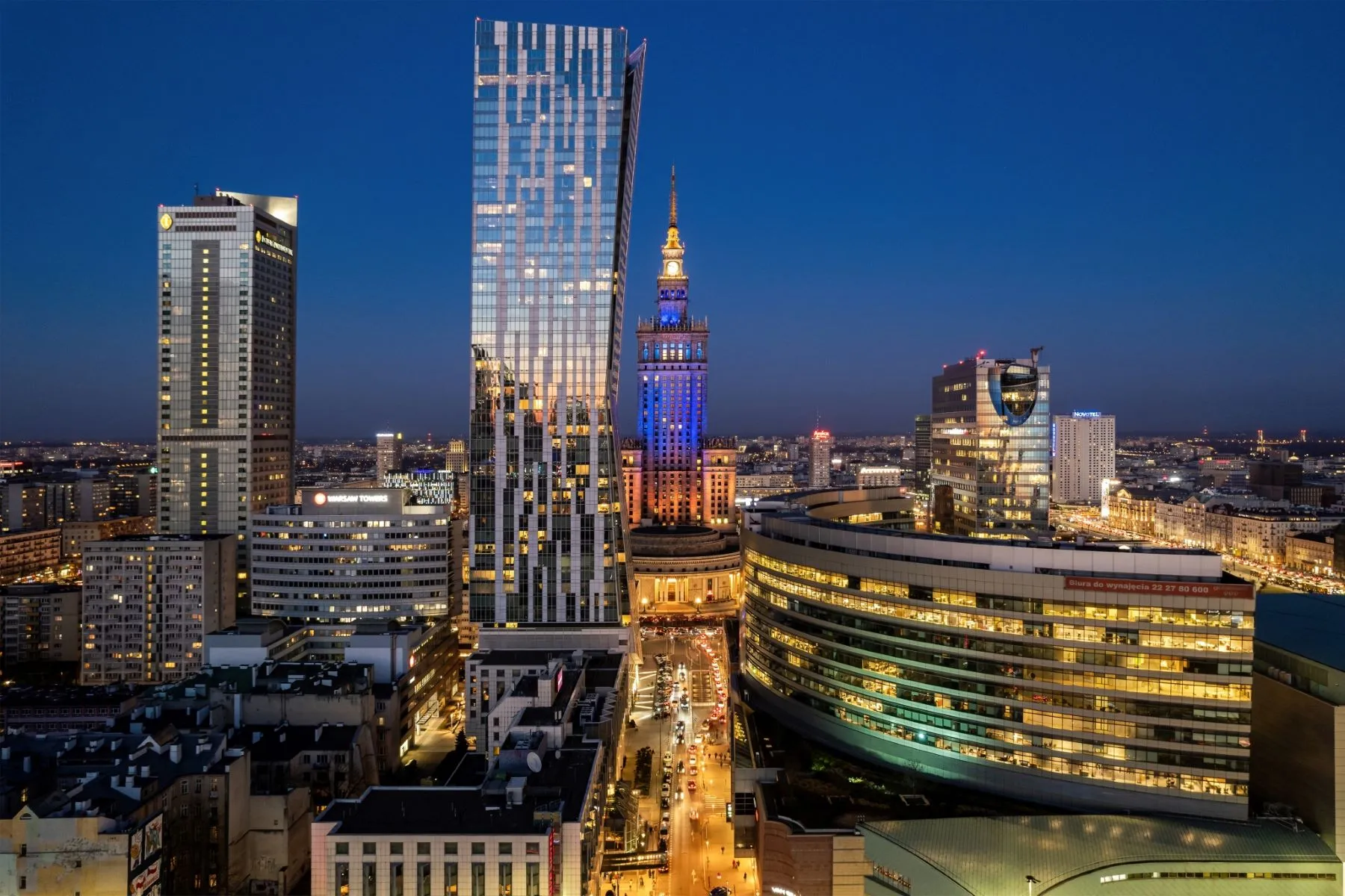Central Warsaw skyline at dusk with illuminated towers and the Palace of Culture and Science