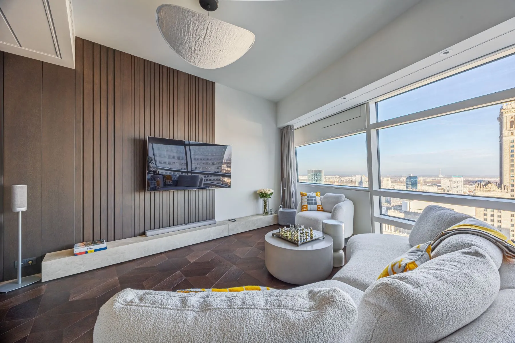 Curved cream sofa facing a wall-mounted television and full-height timber panelling
