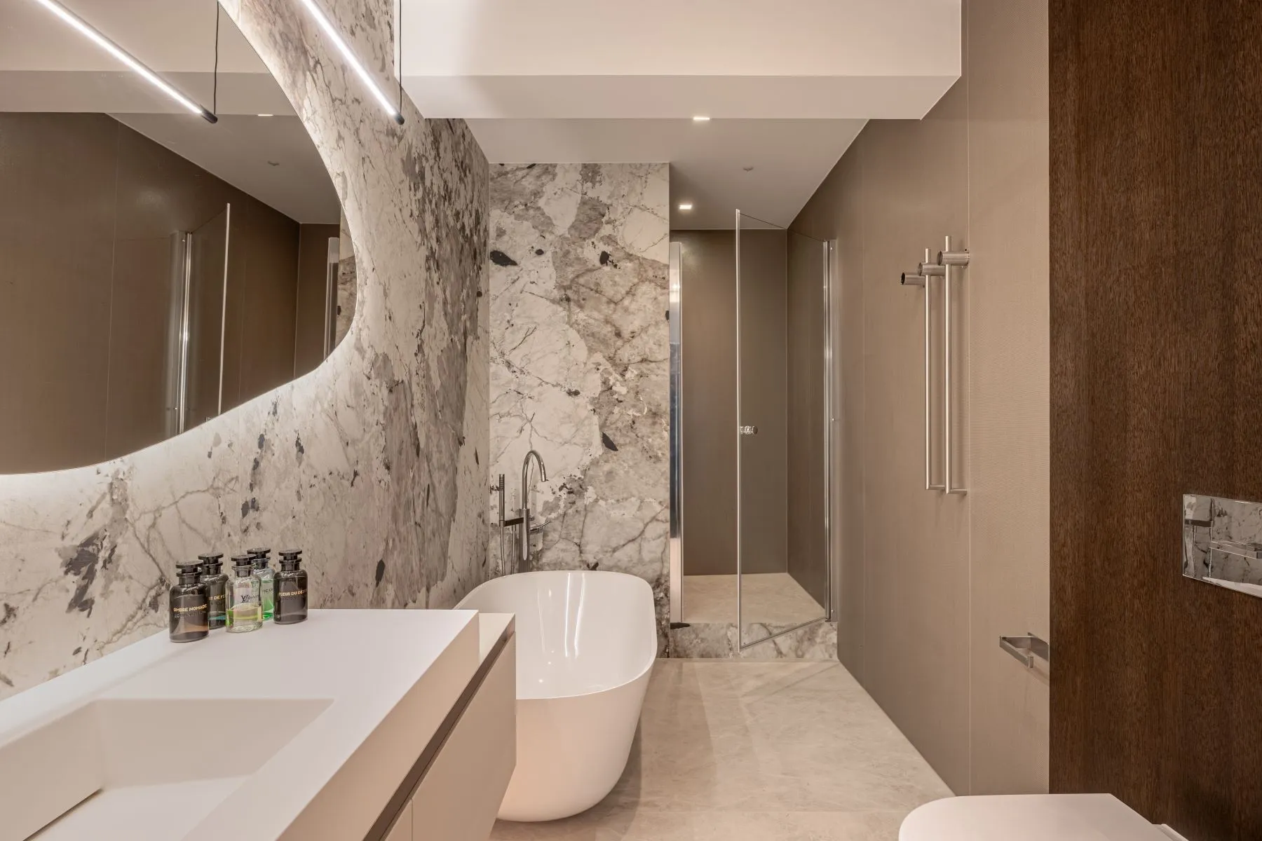Marble-finished bathroom with bathtub, broad vanity and illuminated curved mirror