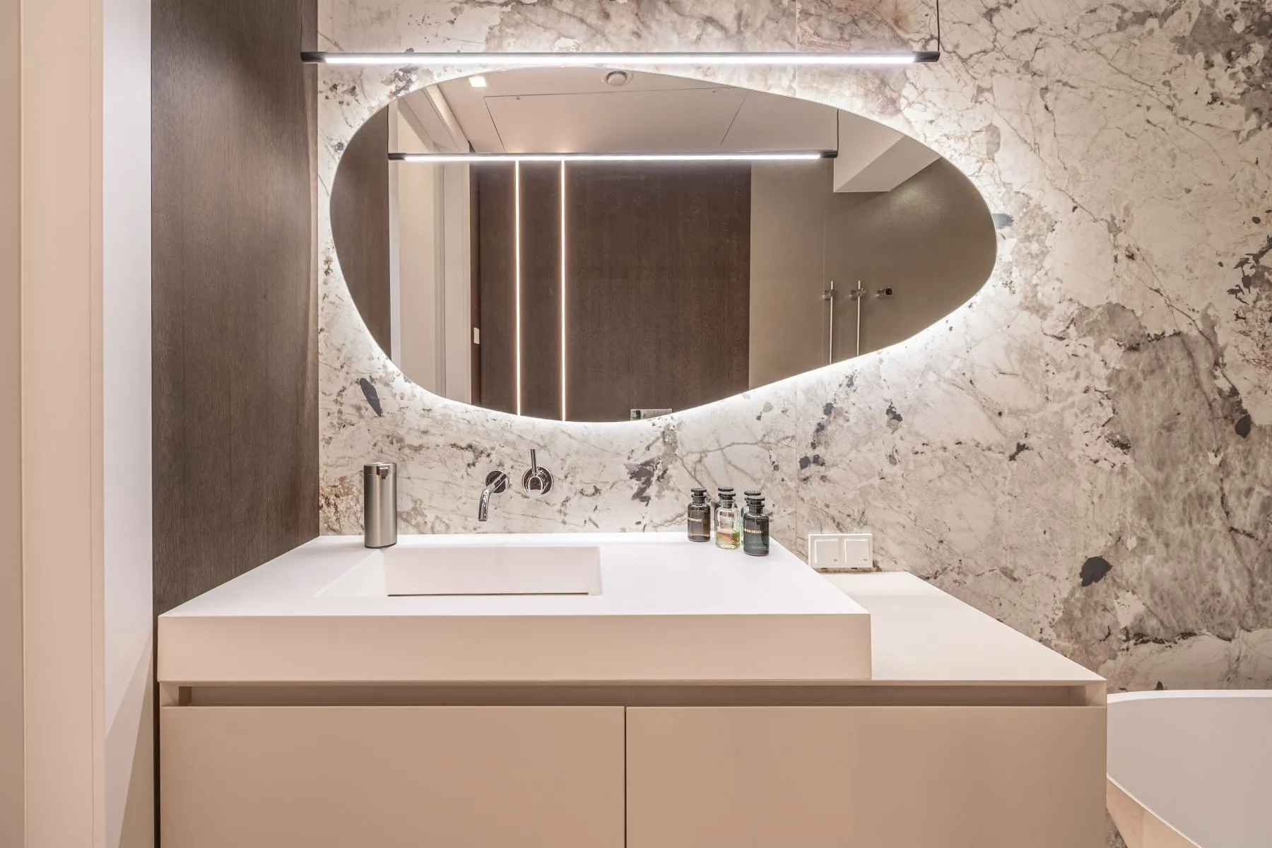 Bathroom vanity with pale cabinetry, stone-patterned wall and sculptural illuminated mirror