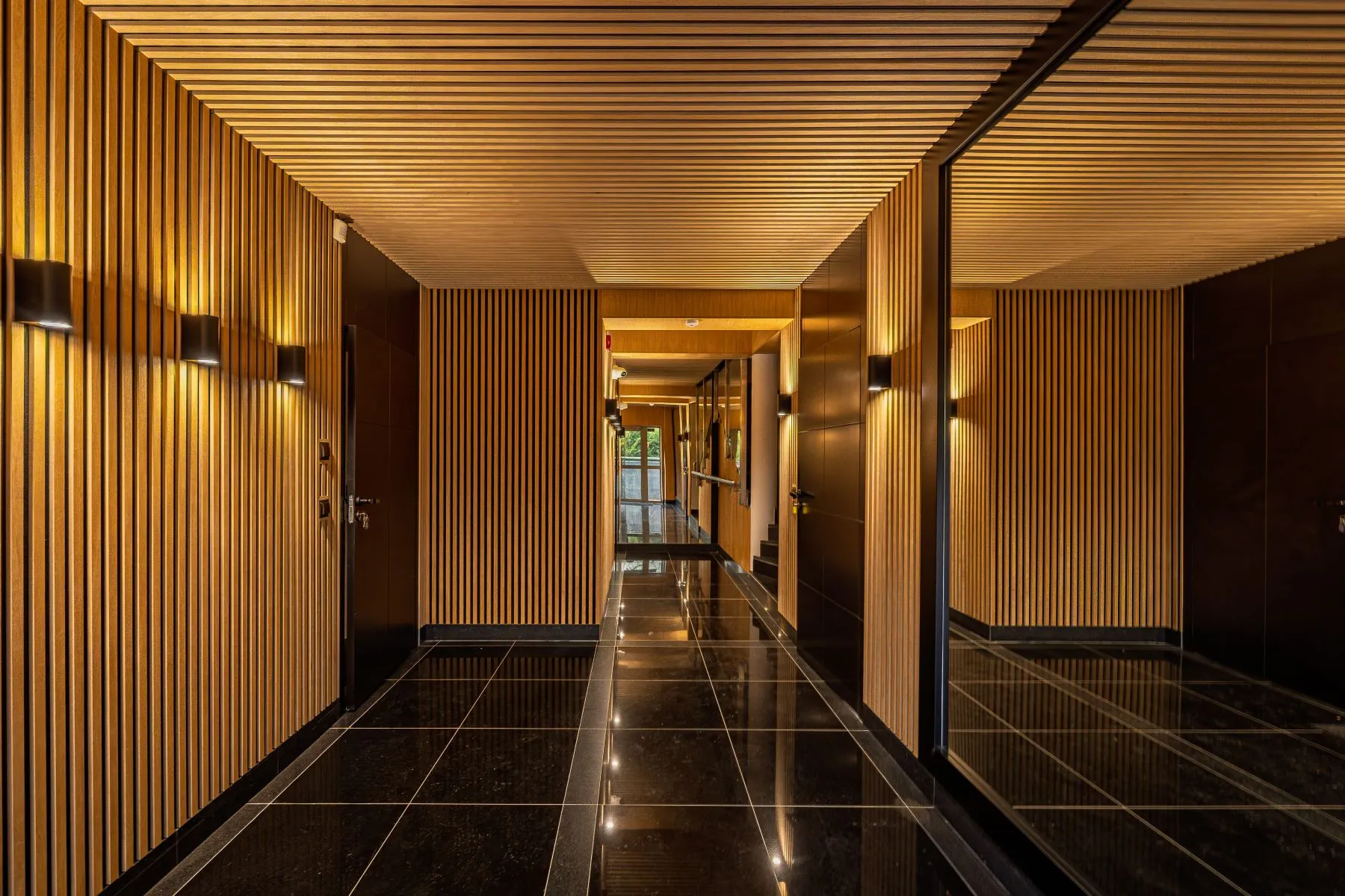 Boutique residence entrance corridor with timber slats, mirrored wall and dark stone flooring