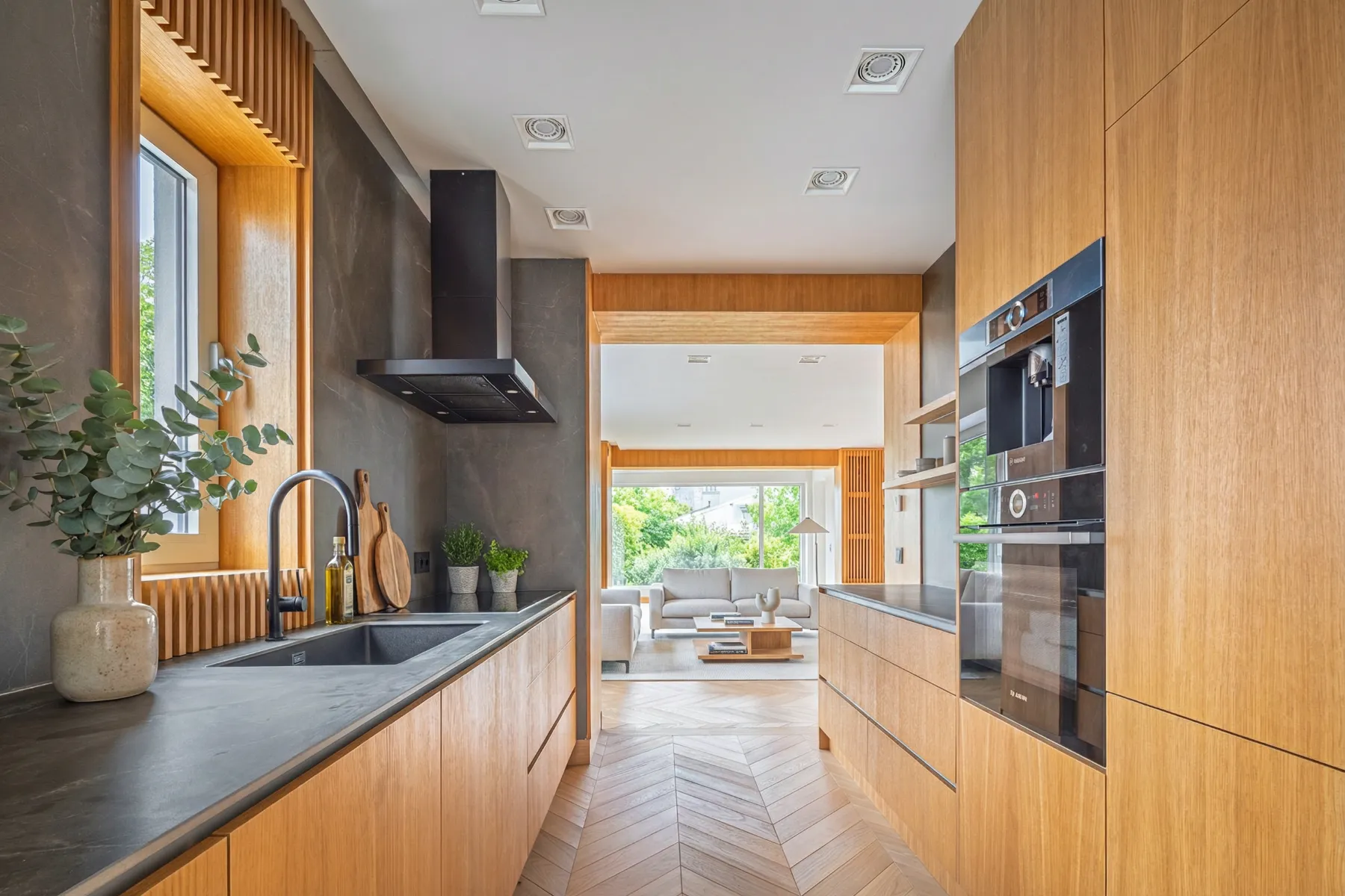 Timber galley kitchen with dark worktops, built-in appliances and herringbone flooring