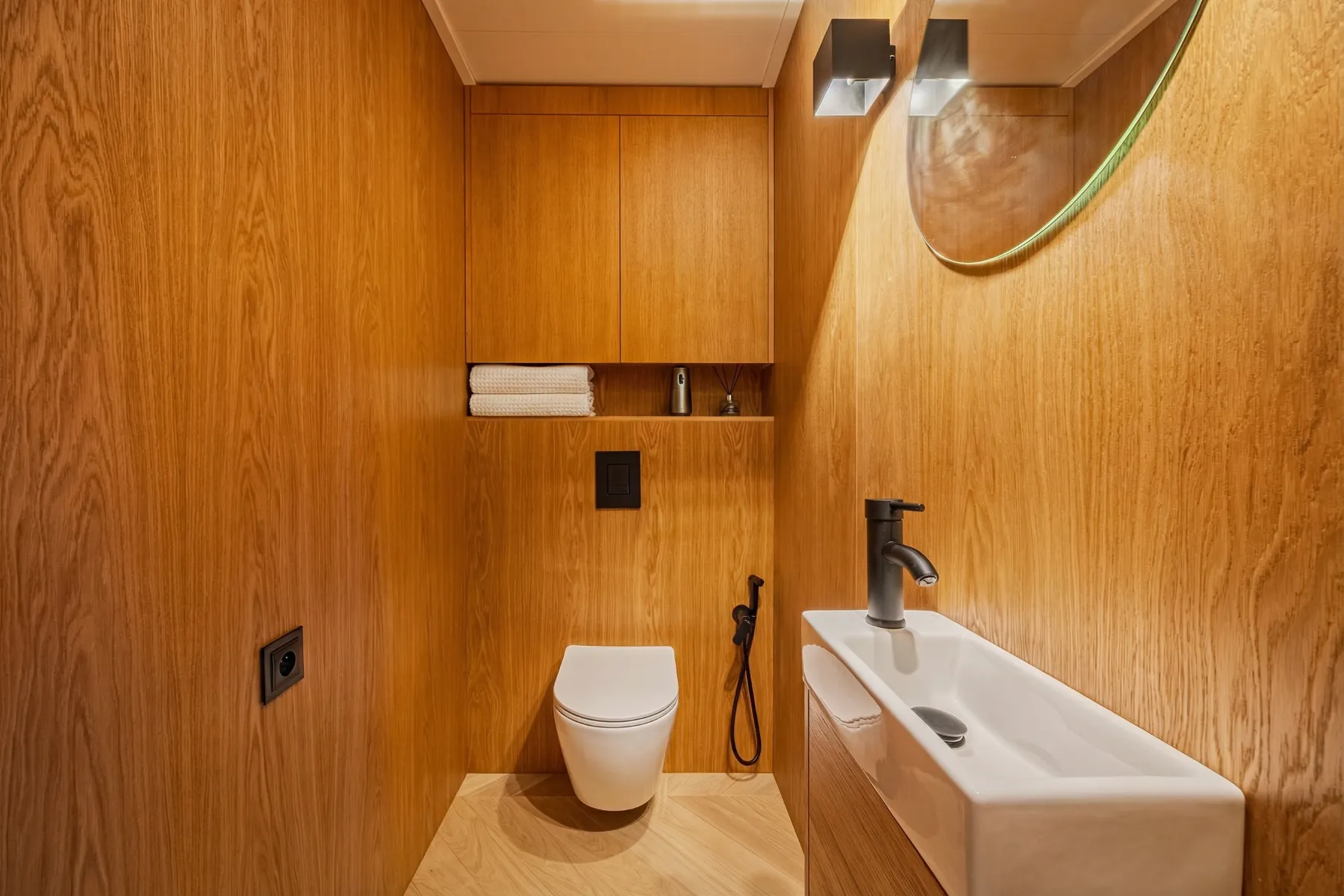 Timber-finished toilet area with wall-hung WC, basin and round mirror