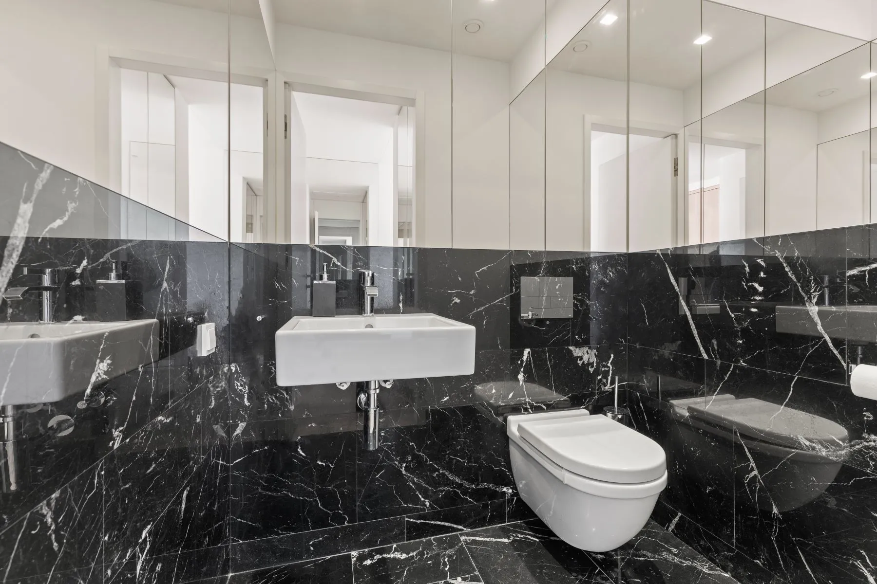Guest cloakroom with black marble-patterned finishes, mirrored cabinets and a wall-mounted basin