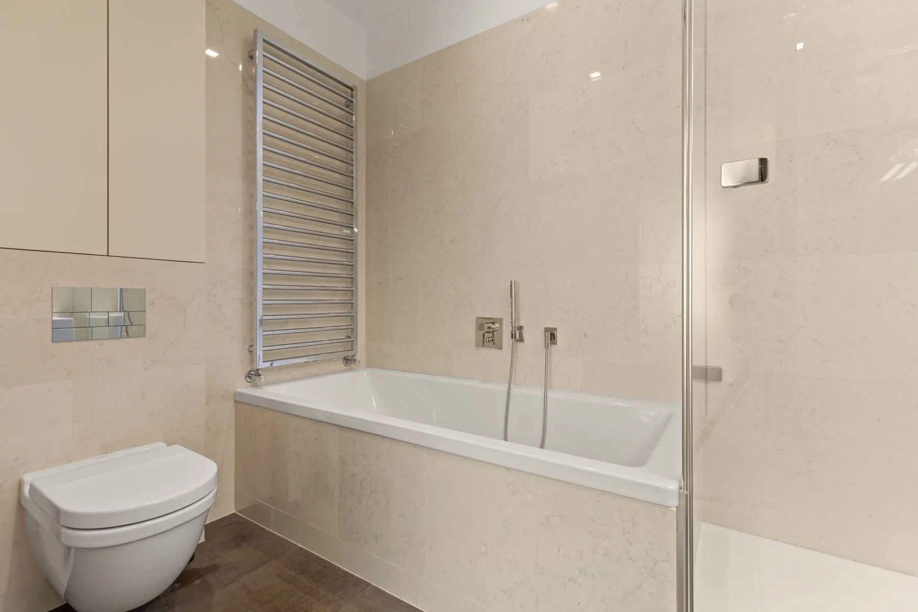 Pale stone-finished bathroom with bathtub, glass shower enclosure and heated towel rail