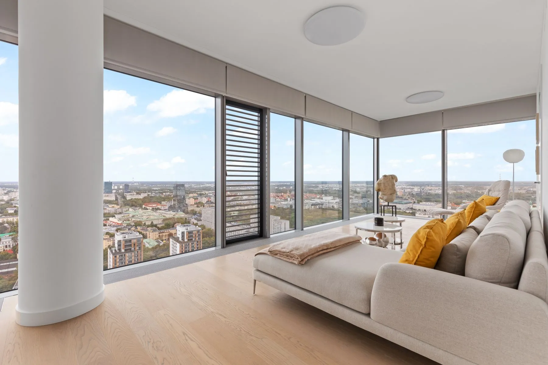 Light grey sectional sofa with yellow cushions beside wraparound skyline-facing windows