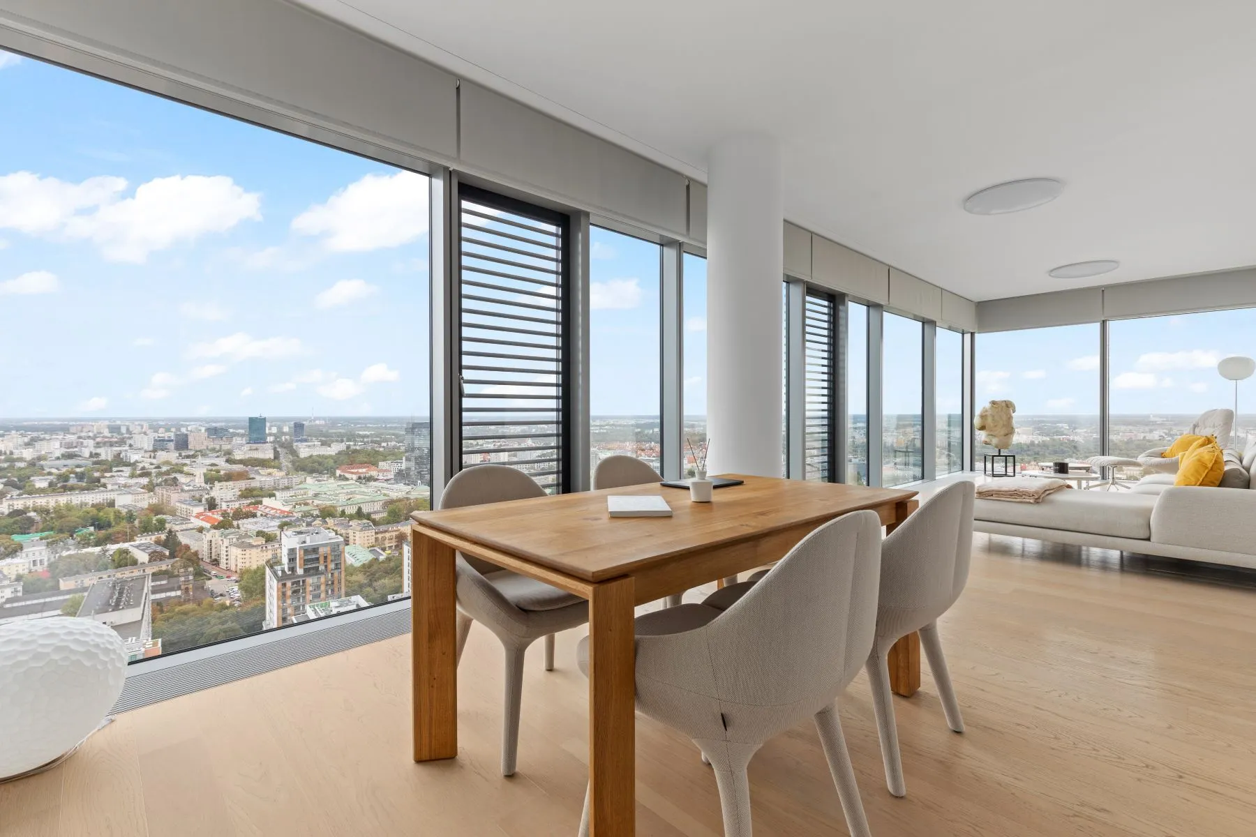 Timber dining table with upholstered chairs overlooking Warsaw through full-height windows