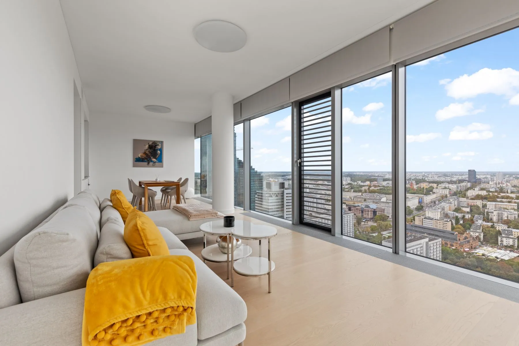 Grey sofa with mustard cushions and throw facing glass coffee tables and the city panorama