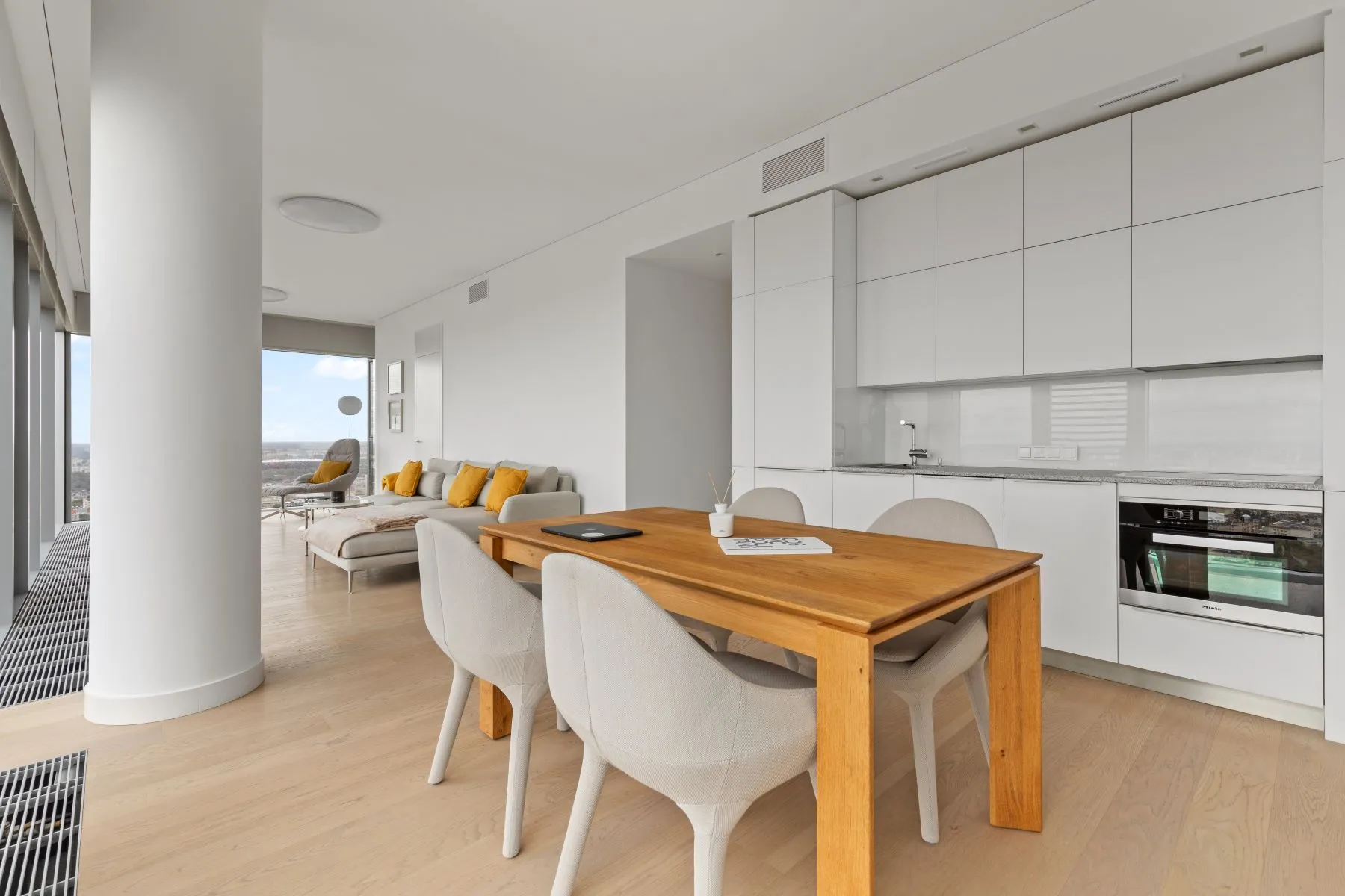 Open kitchen with white cabinetry and a built-in oven beside the timber dining table
