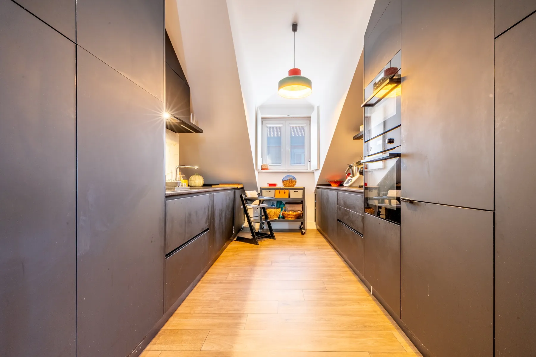 Long contemporary galley kitchen with dark cabinetry and dining area