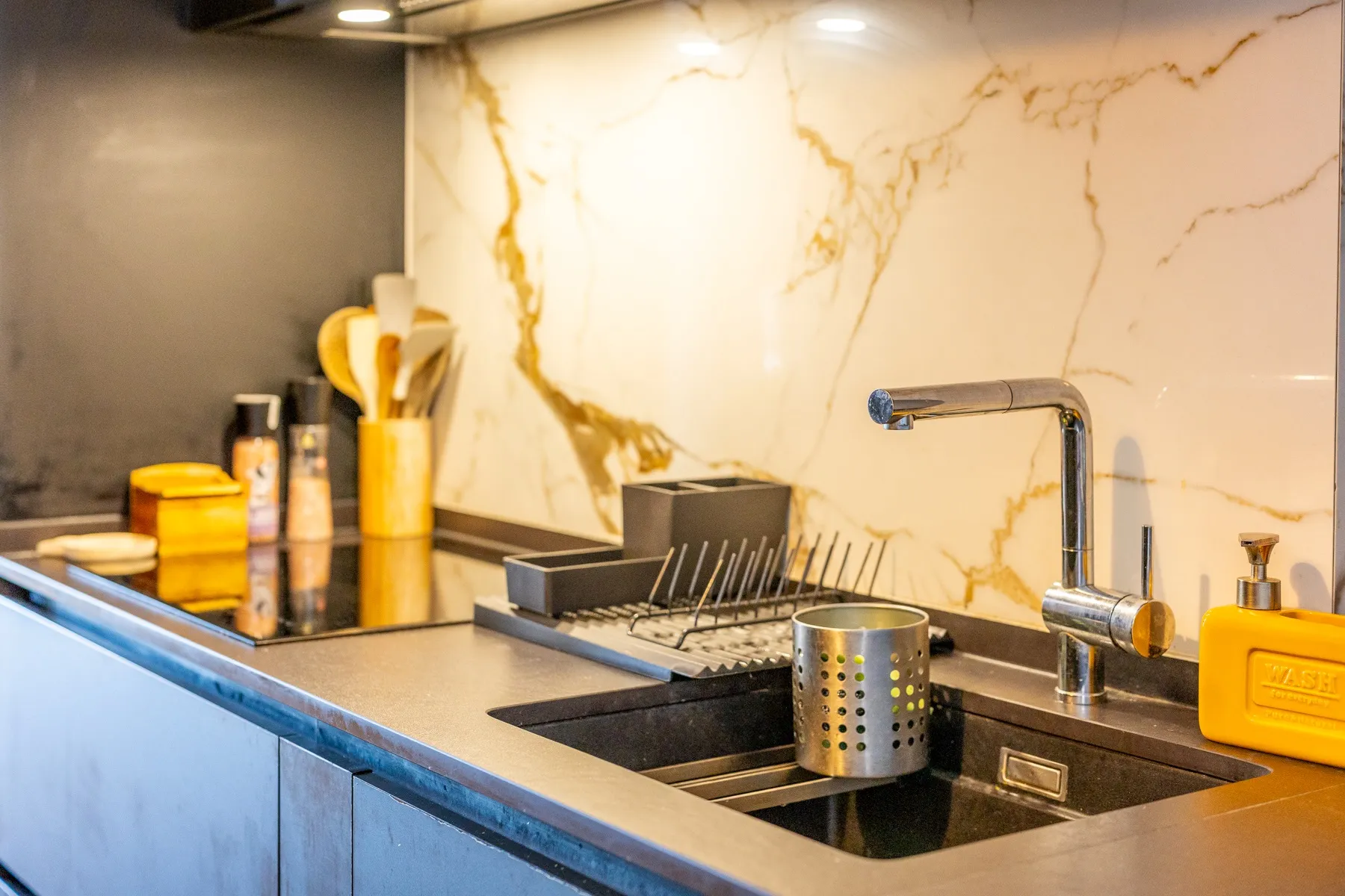 Modern kitchen sink and marble-effect splashback beneath fitted lighting