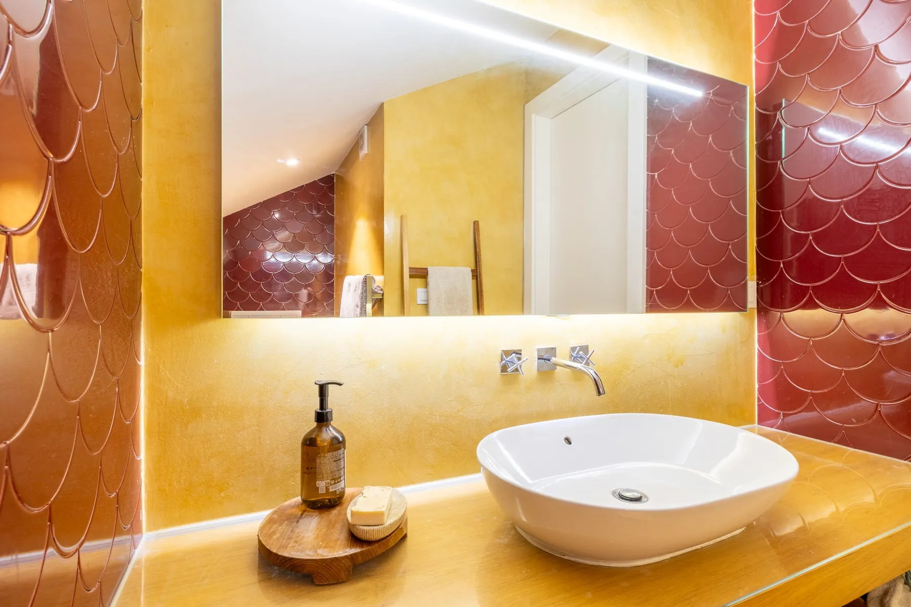 Sculptural basin and broad mirror in the colourful en-suite bathroom