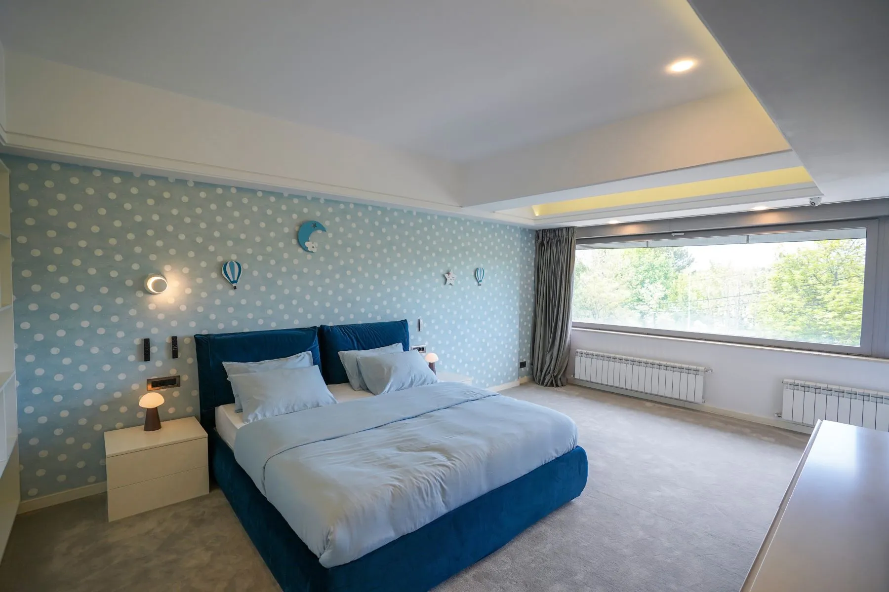 Spacious double bedroom with blue upholstered bed and wide garden-facing window