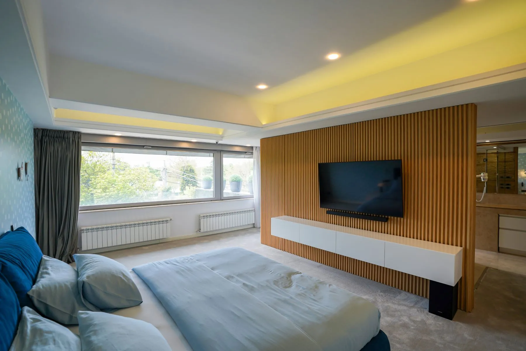 Double bedroom with blue bed, timber media wall and recessed lighting