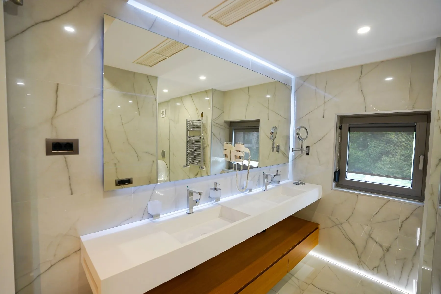 Bright marble bathroom with broad double vanity and illuminated wall mirror