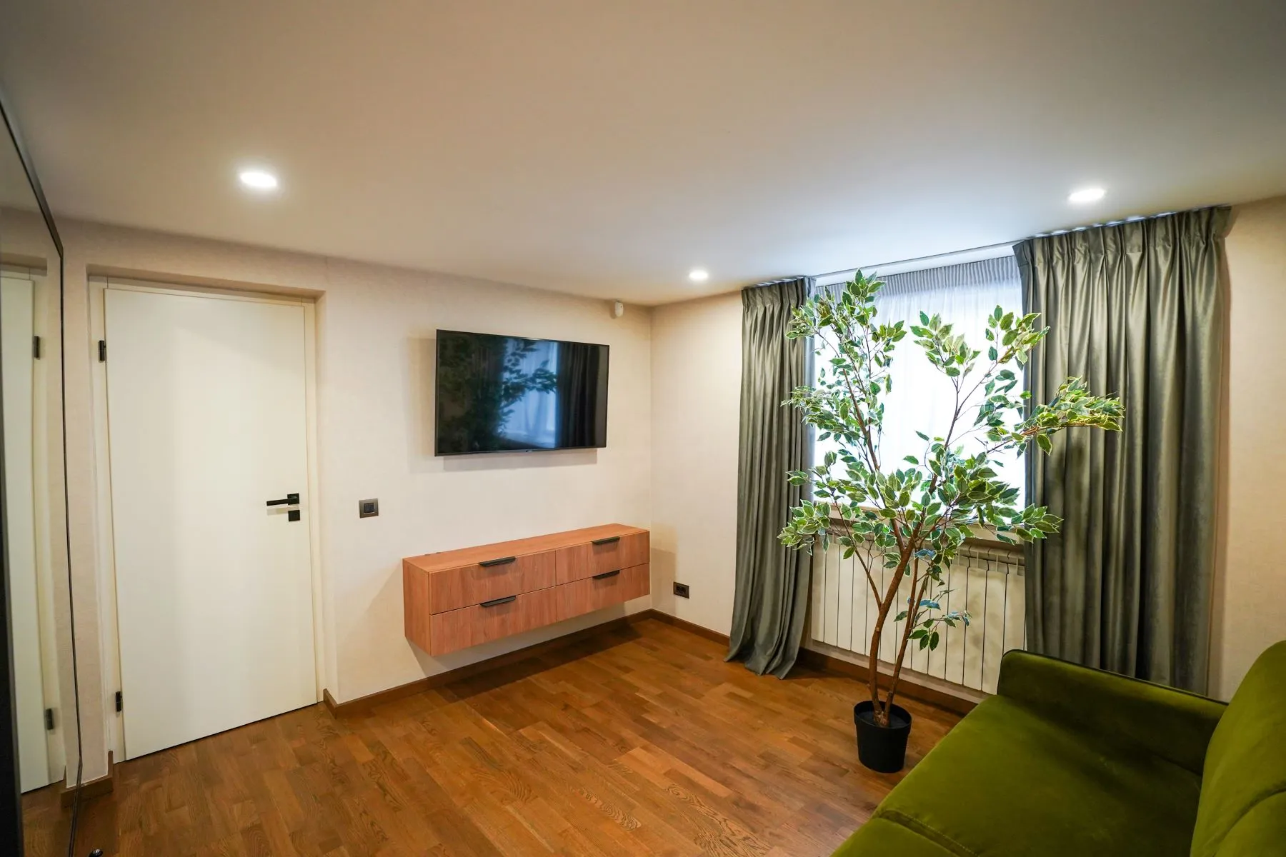 Flexible guest lounge with green sofa, television and garden-facing window