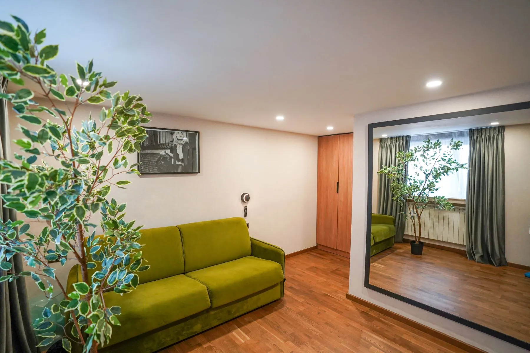 Private guest sitting room with green sofa, full-height mirror and timber flooring
