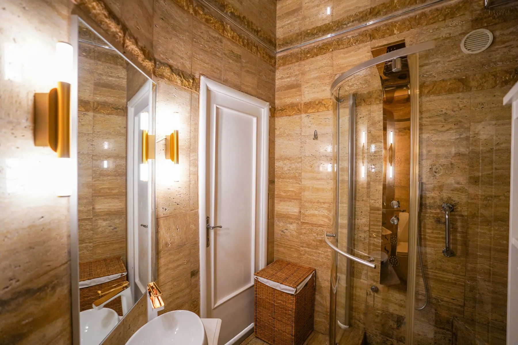 Polished stone bathroom with glass-enclosed shower and warm wall lighting