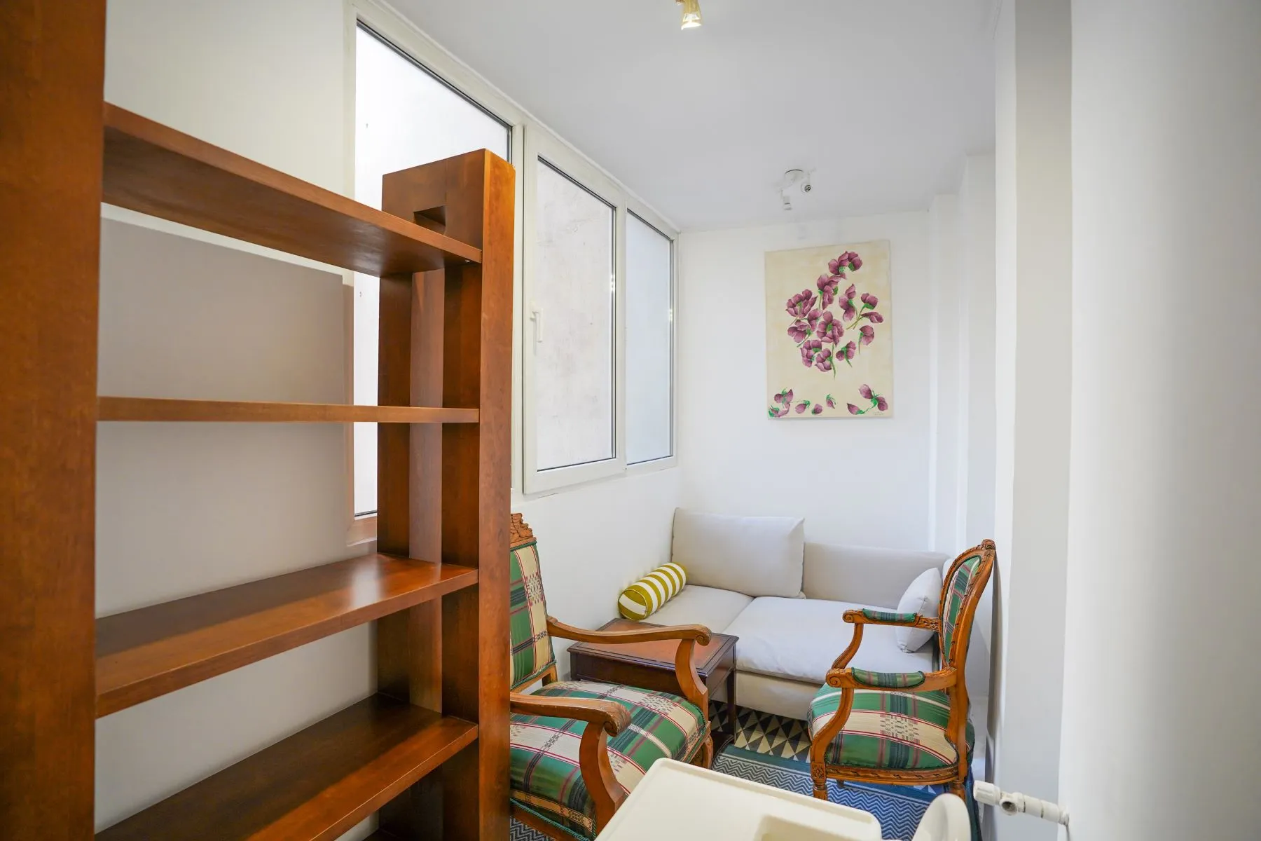 Enclosed loggia with colourful period armchairs, artwork and open shelving