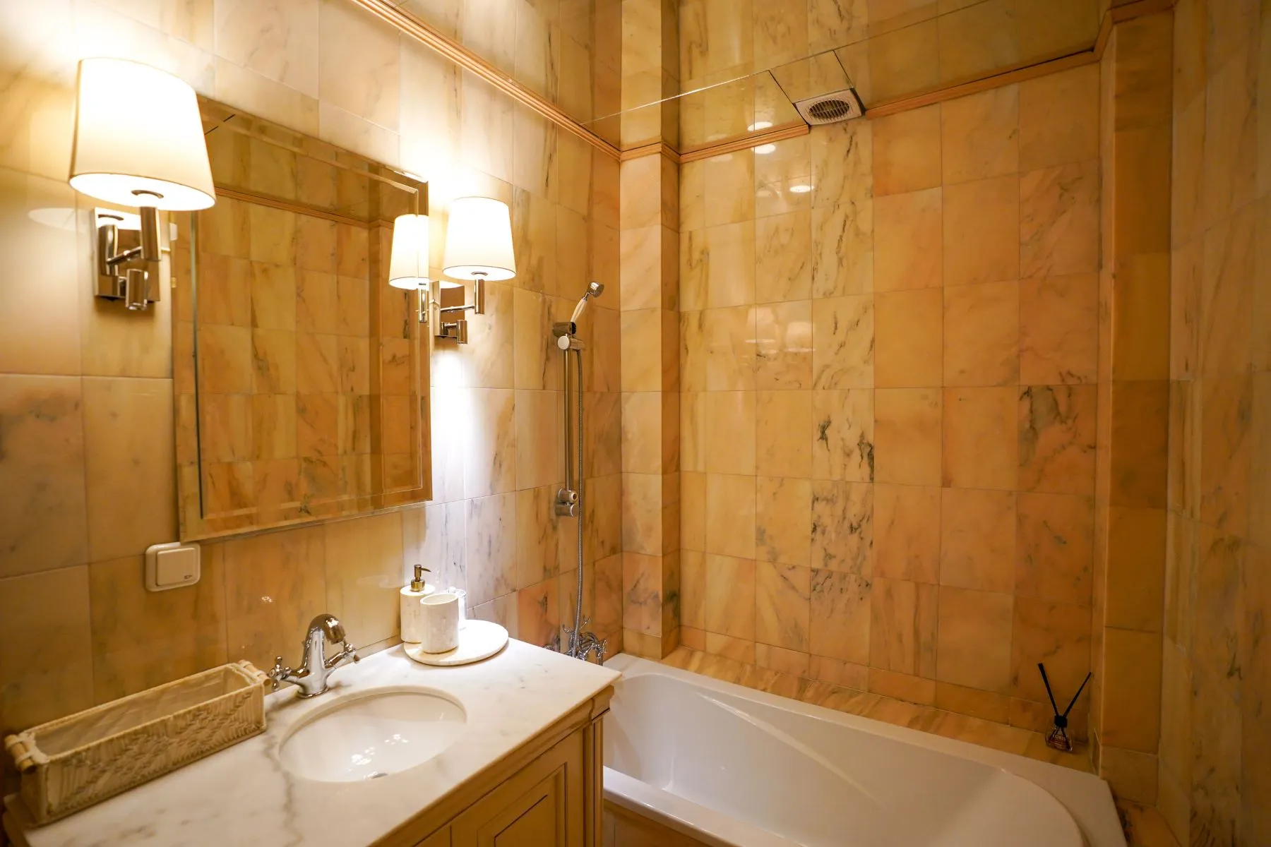 Marble-finished bathroom with bathtub, shower fittings and illuminated vanity