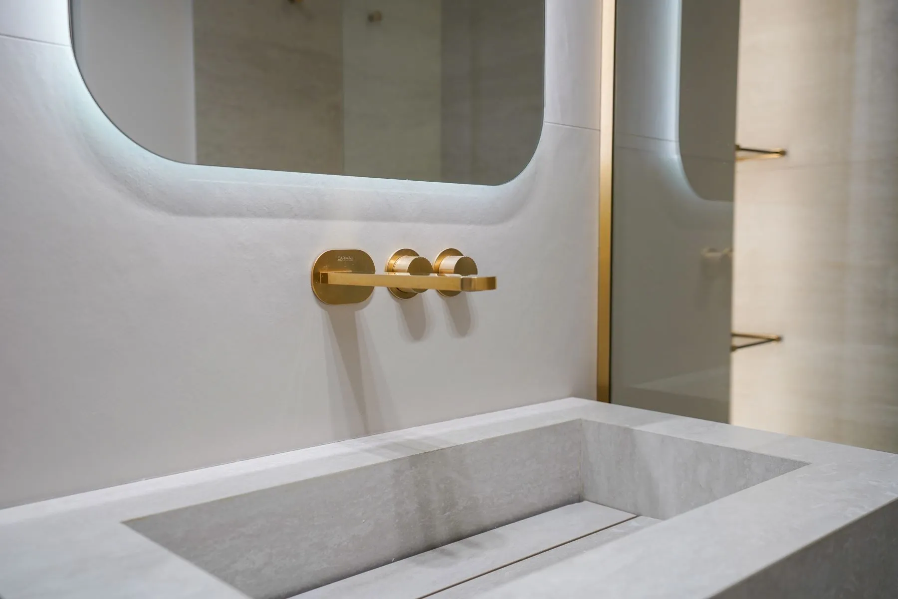 Stone vanity basin with gold fittings beneath a softly illuminated mirror