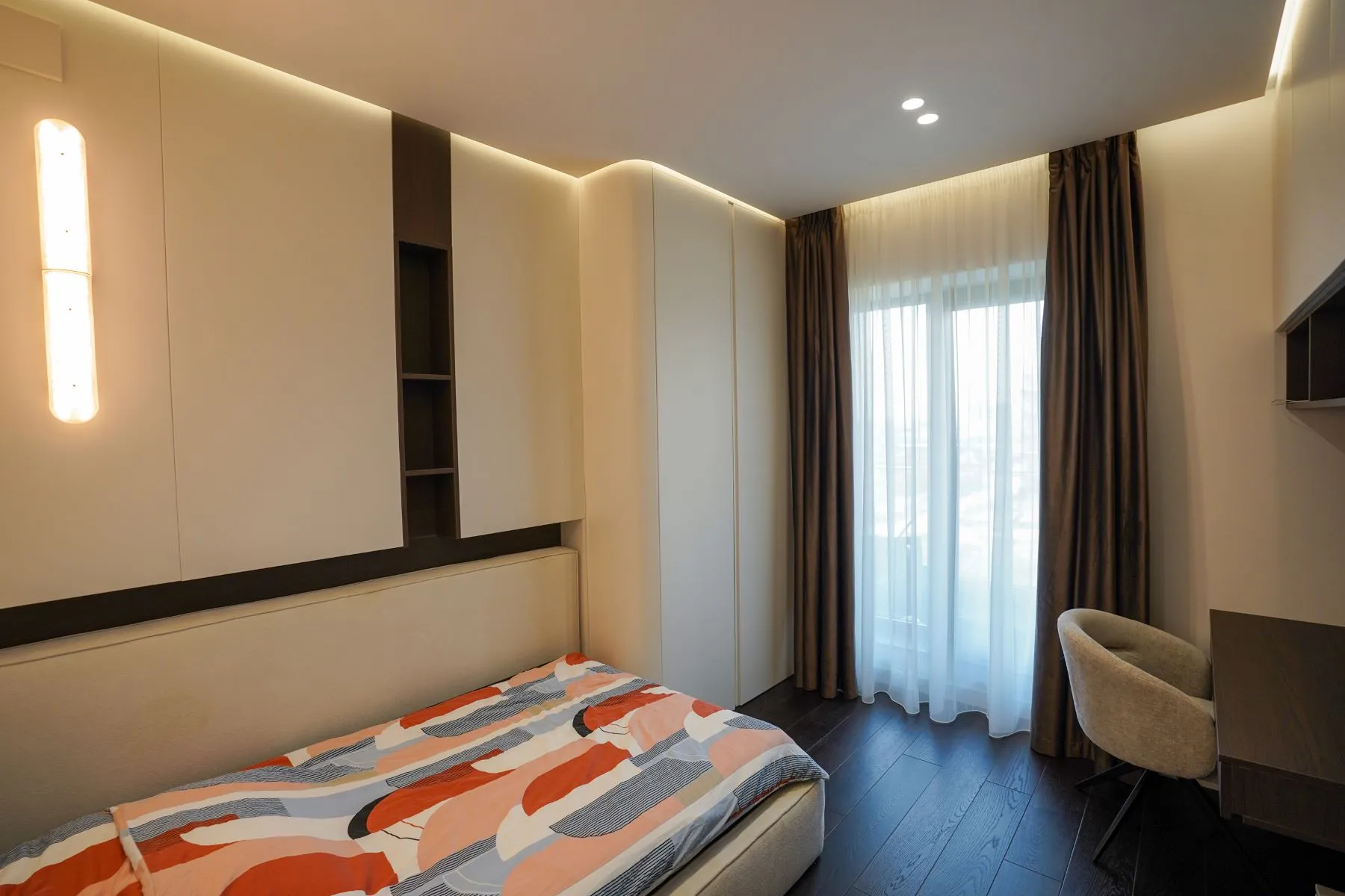 Furnished guest bedroom with colourful bedding, fitted storage and study desk