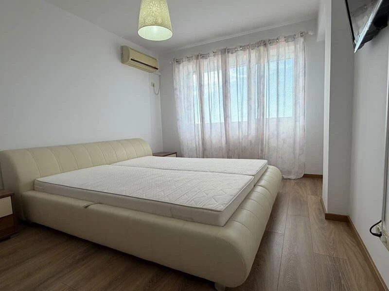 Double bedroom with cream upholstered bed and wide city-facing window