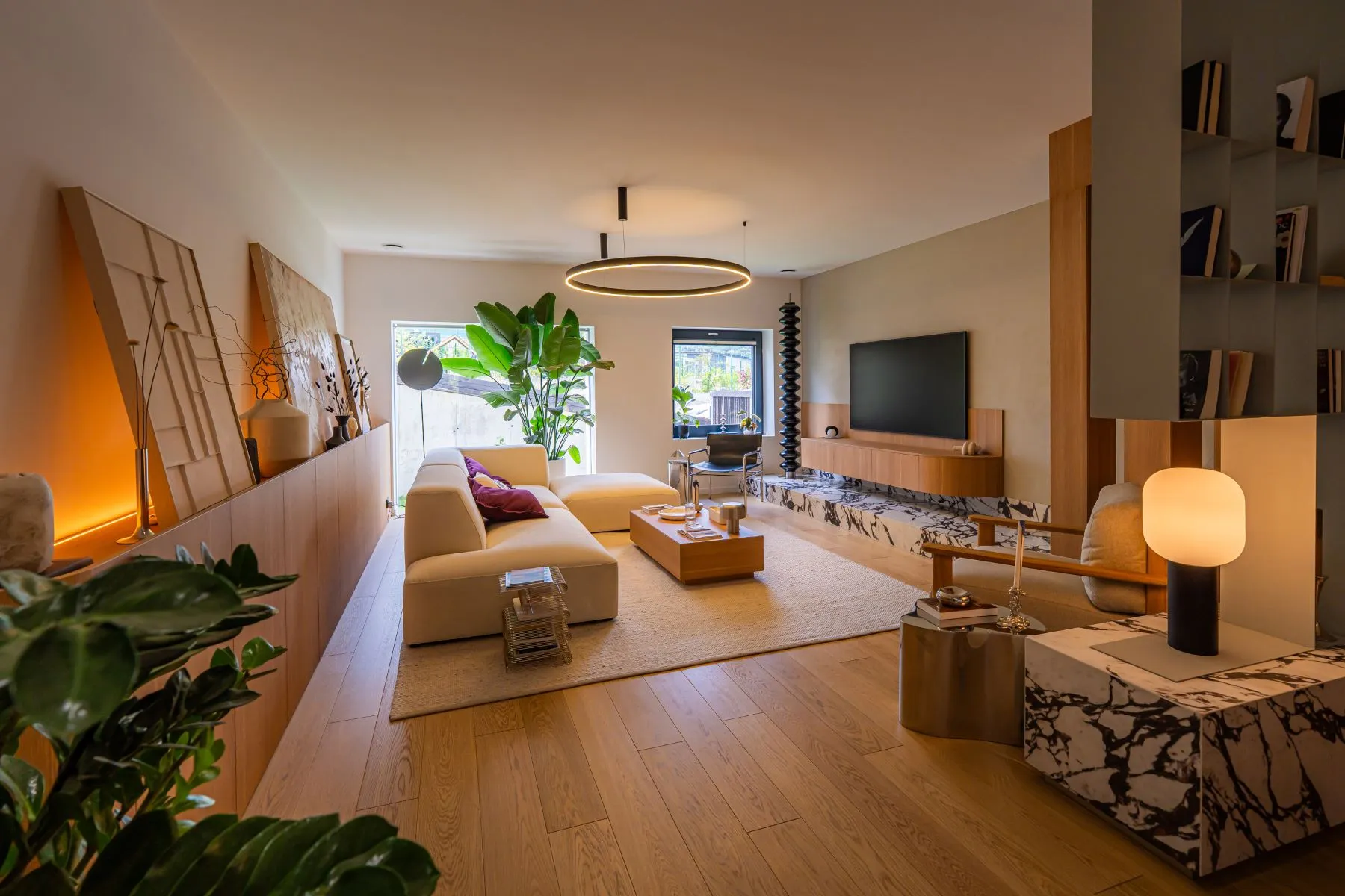 Long open-plan lounge with television wall, artwork and natural timber flooring