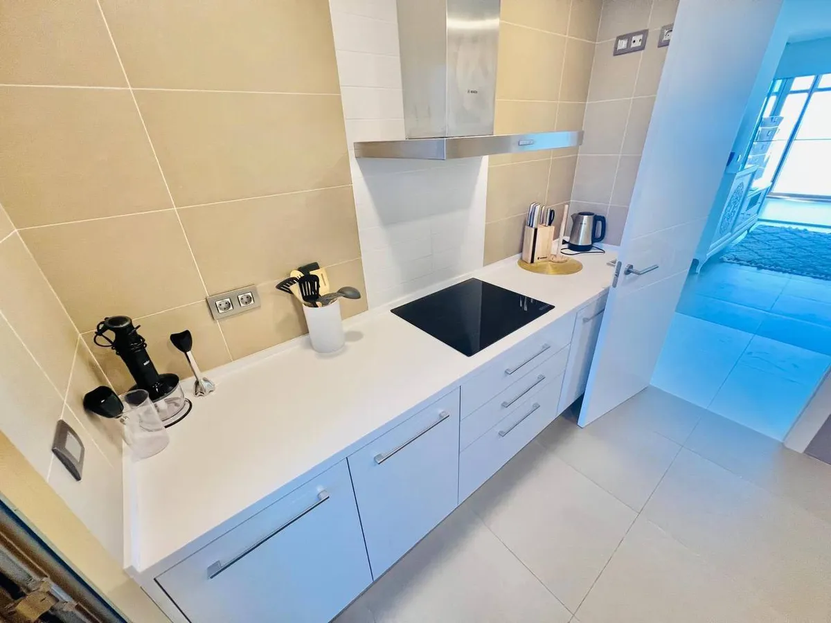 Compact white fitted kitchen with ceramic hob and Mediterranean view beyond