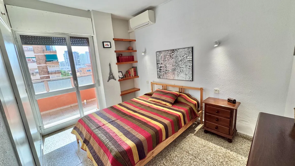 Double bedroom with striped bedspread and balcony-facing windows