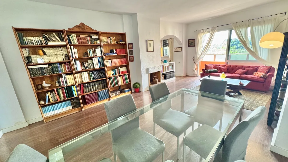 Glass dining table beside full bookcases in the bright principal living room